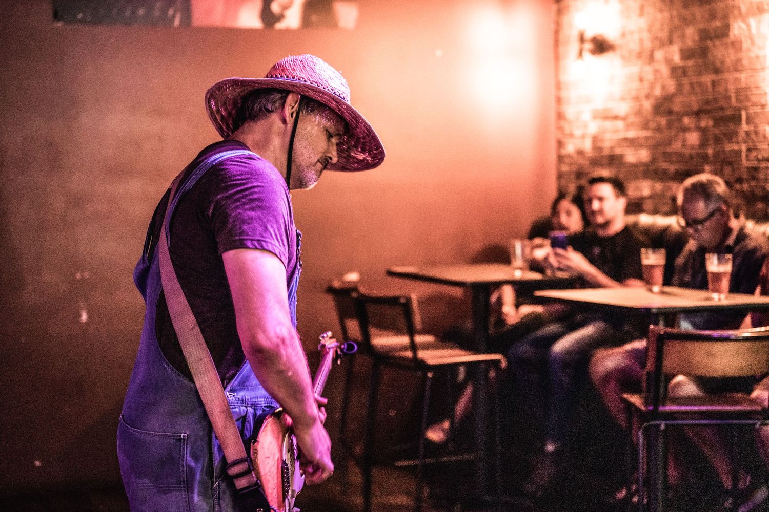 Performer in straw hat plays music in small venue with seated audience visible.