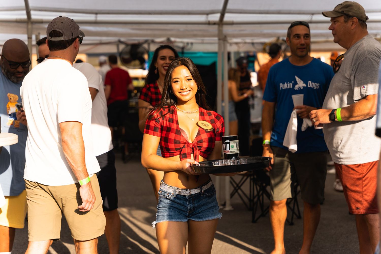 Casual crowd gathering at an outdoor festival under white tents.
