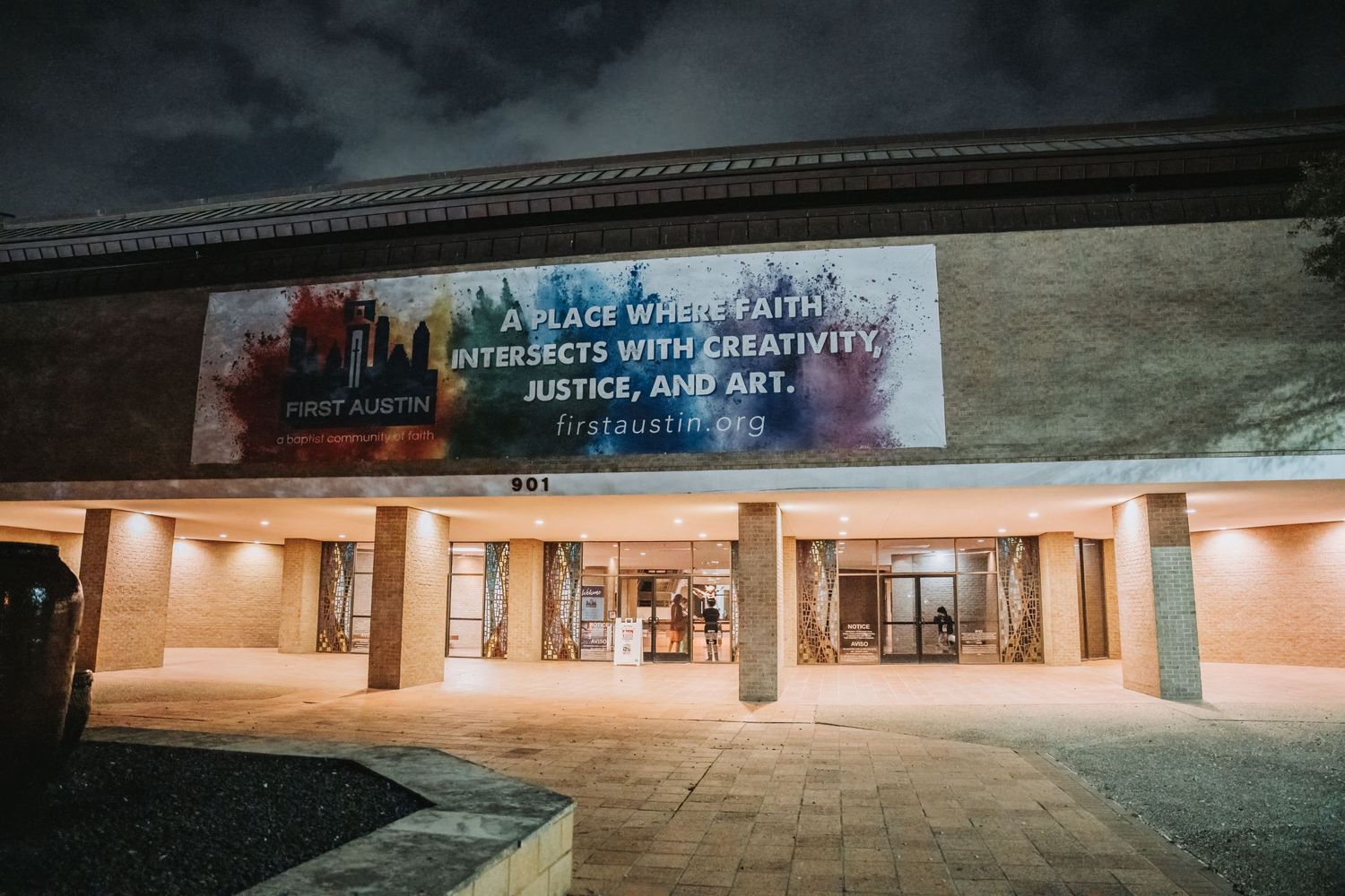 Illuminated theater entrance at night with a banner displayed above the doorway.