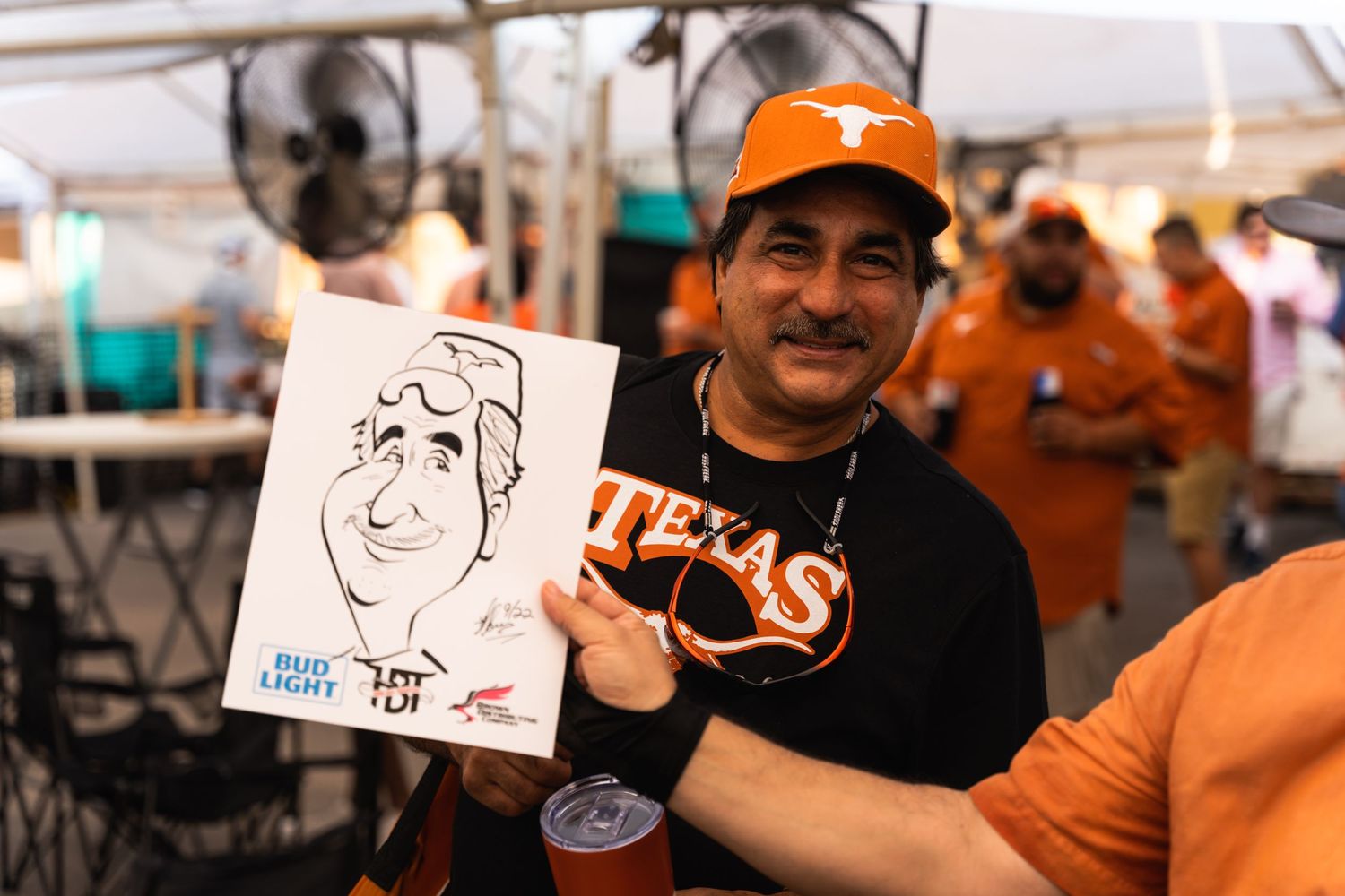 A person in a Texas shirt displays a caricature drawing at an outdoor event.