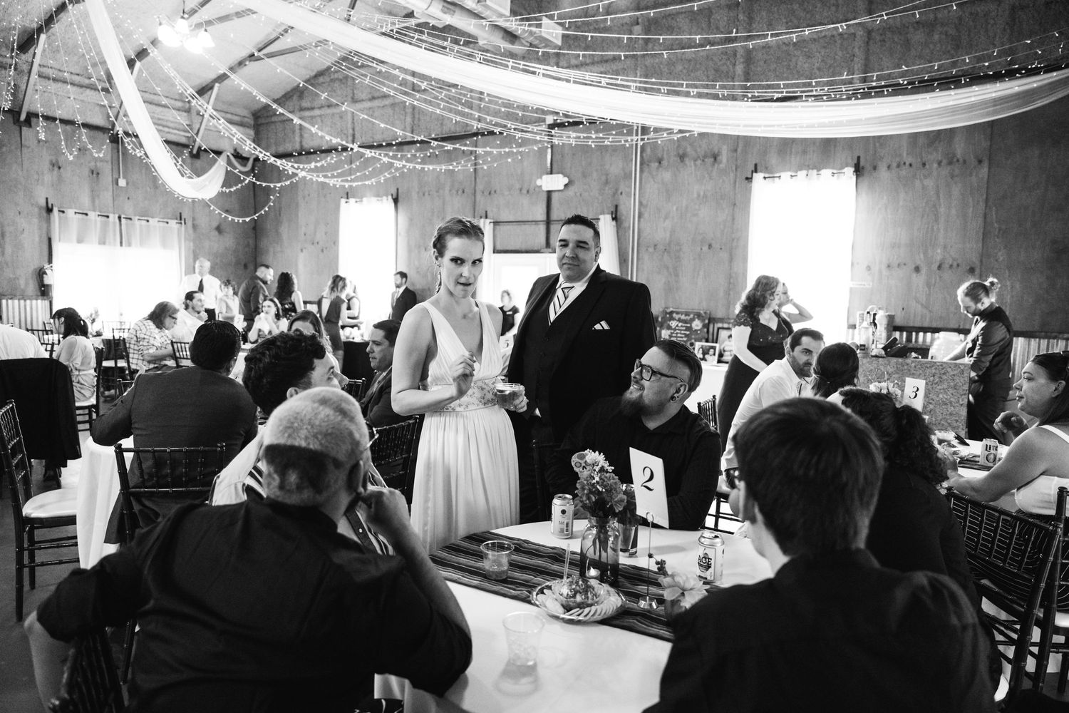 A black and white photo of guests celebrating at a wedding reception in a decorated venue.