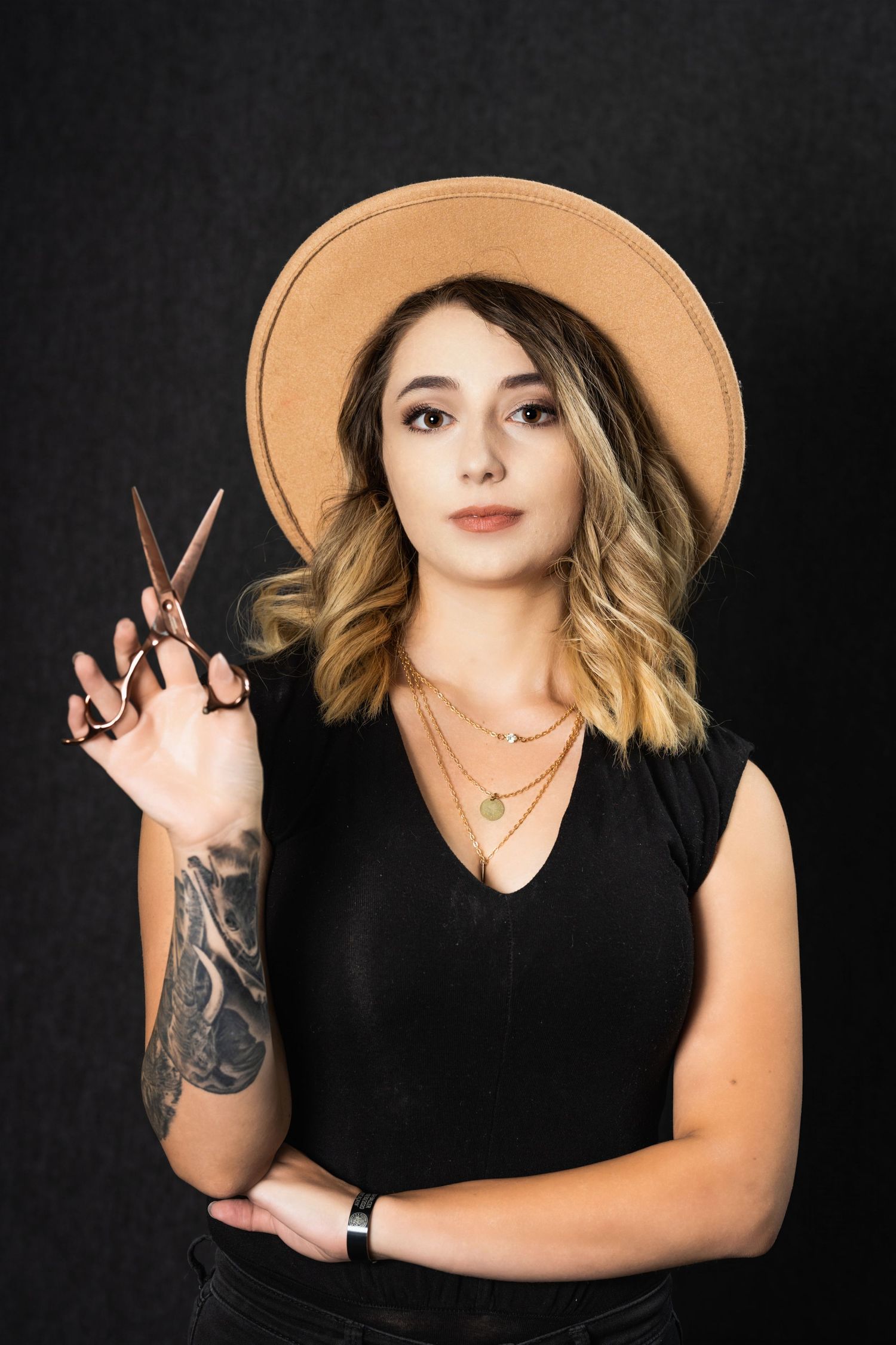 Professional stylist pose holding scissors with tan hat and sleeve tattoo.