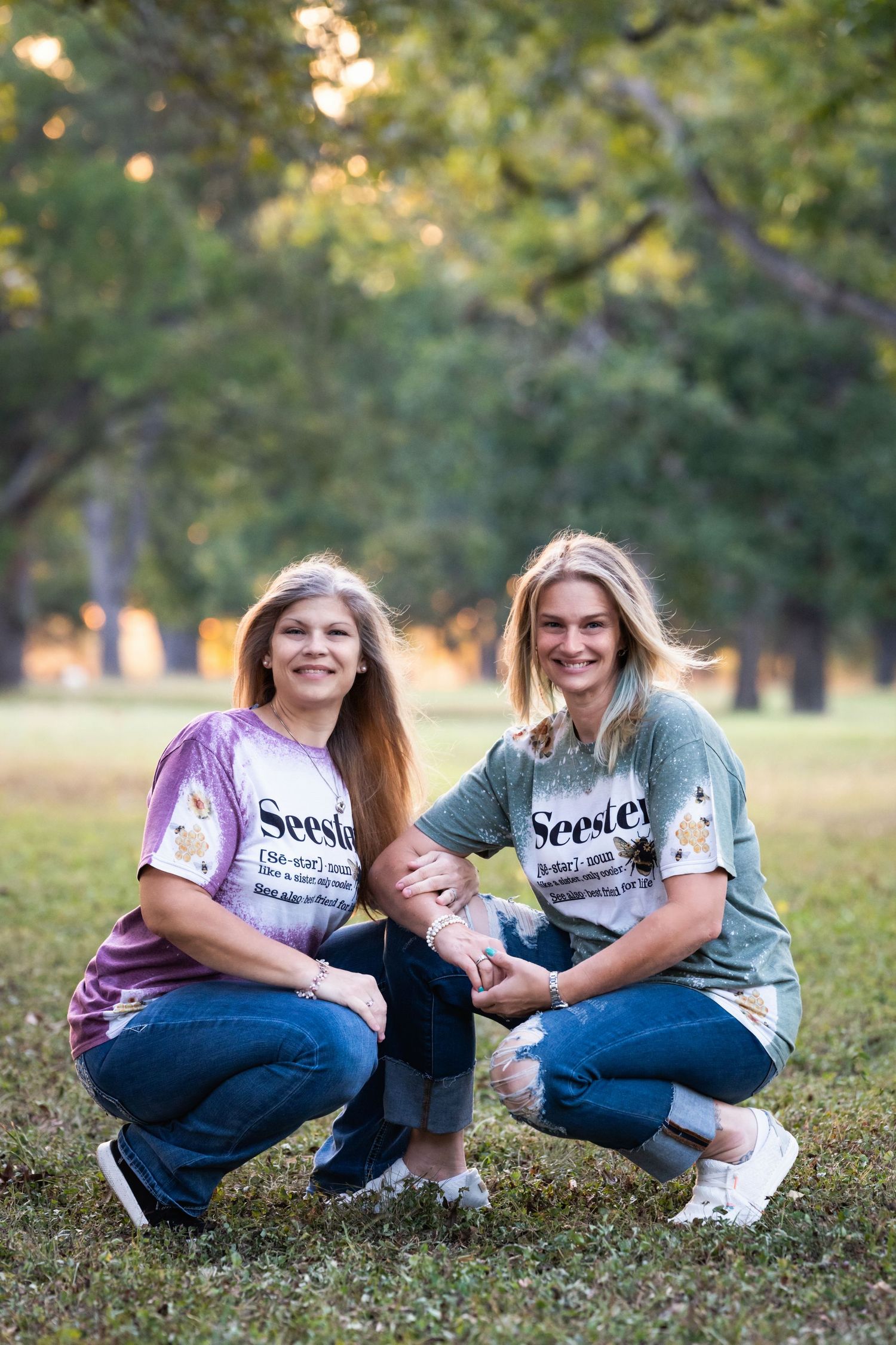 Two people in tie-dye shirts kneel with a small child in a grassy outdoor setting.
