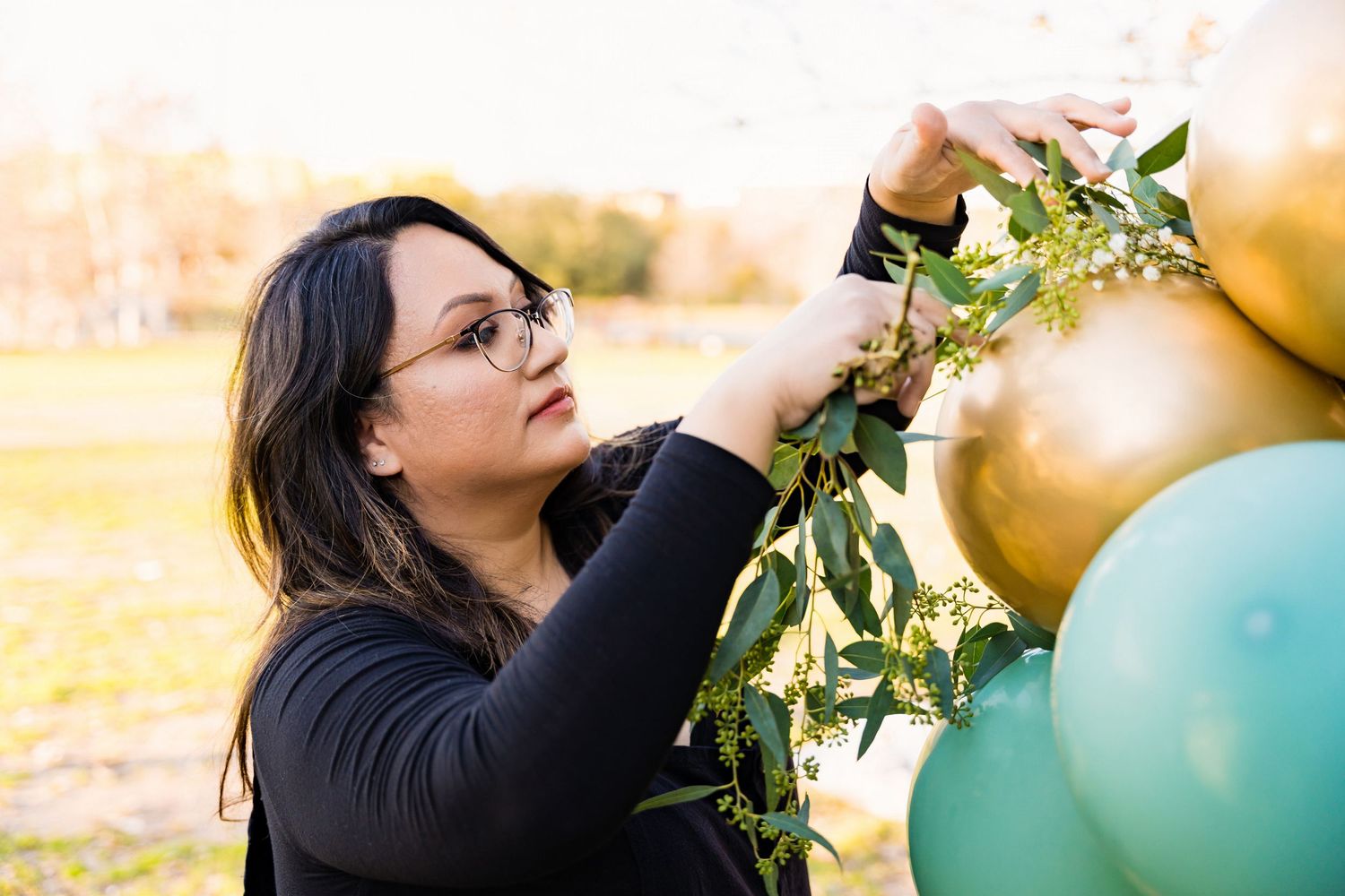 Person adding floral decorations to a balloon installation in an outdoor setting.
