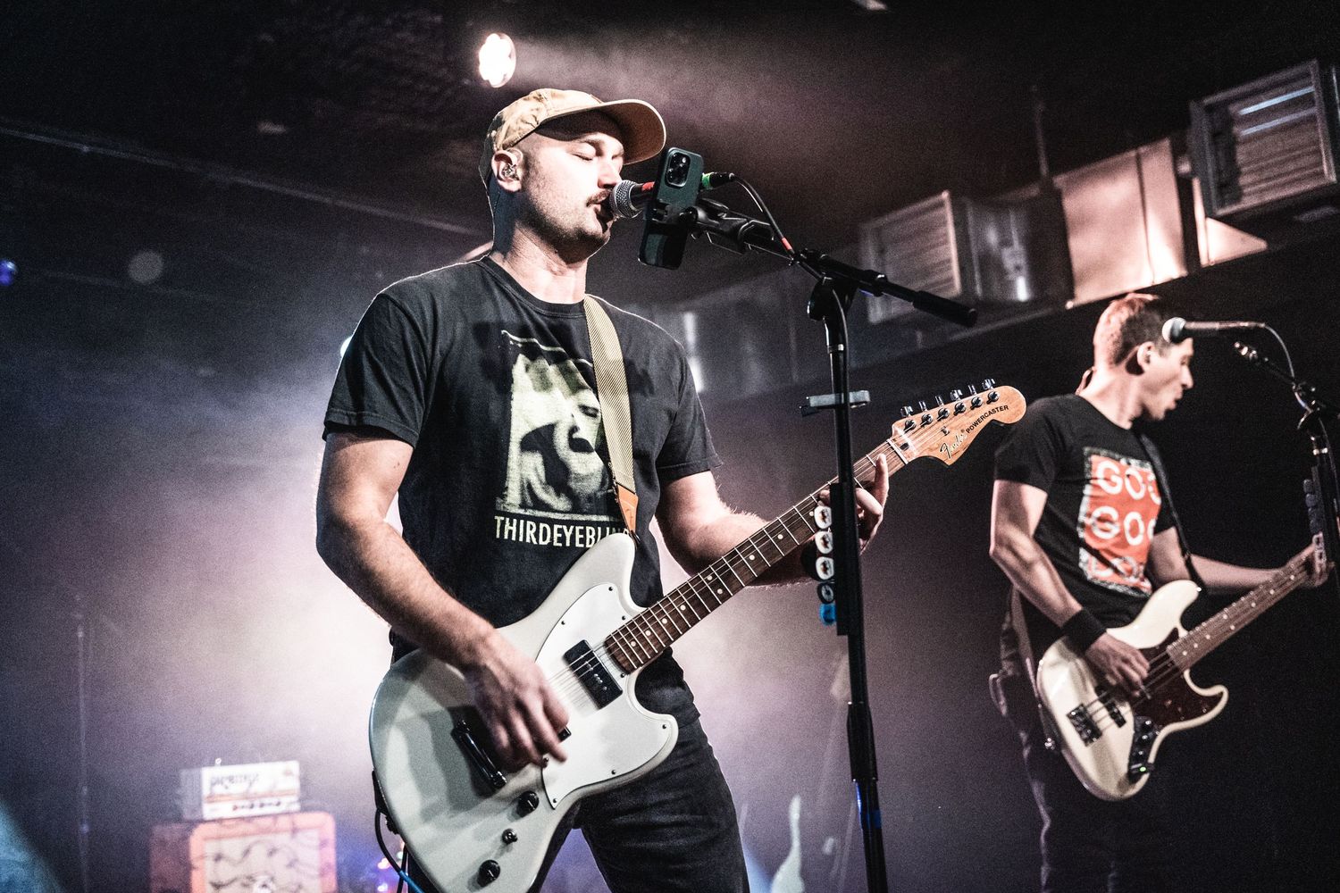 Musicians performing with electric guitars on a concert stage with moody lighting.