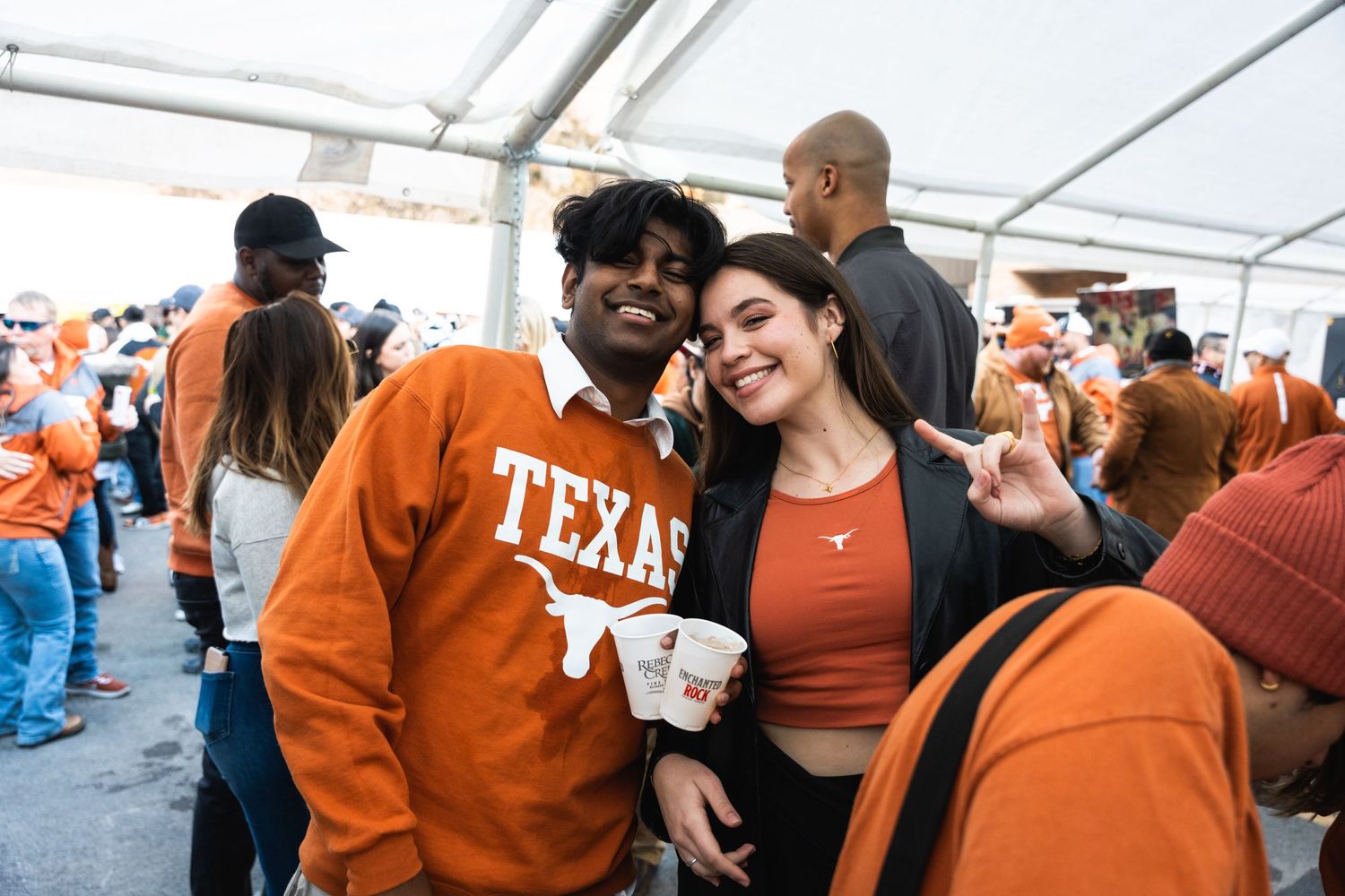 People in Texas orange attire smile together at an outdoor event under a white tent.