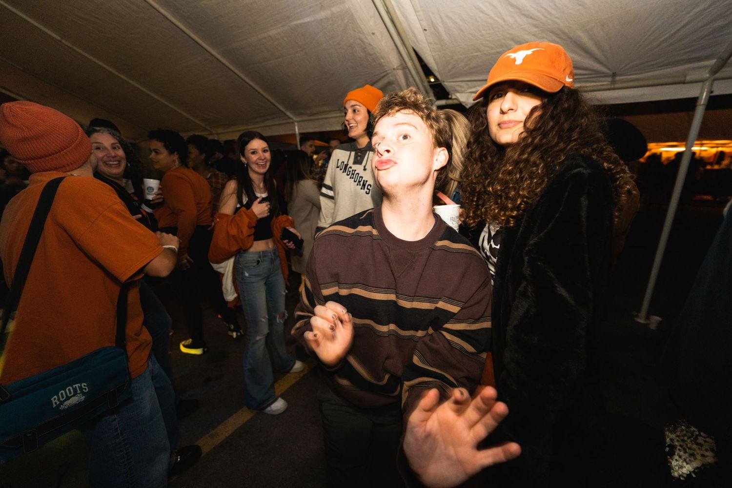 Crowd of partygoers dancing and socializing under tent lighting at night.