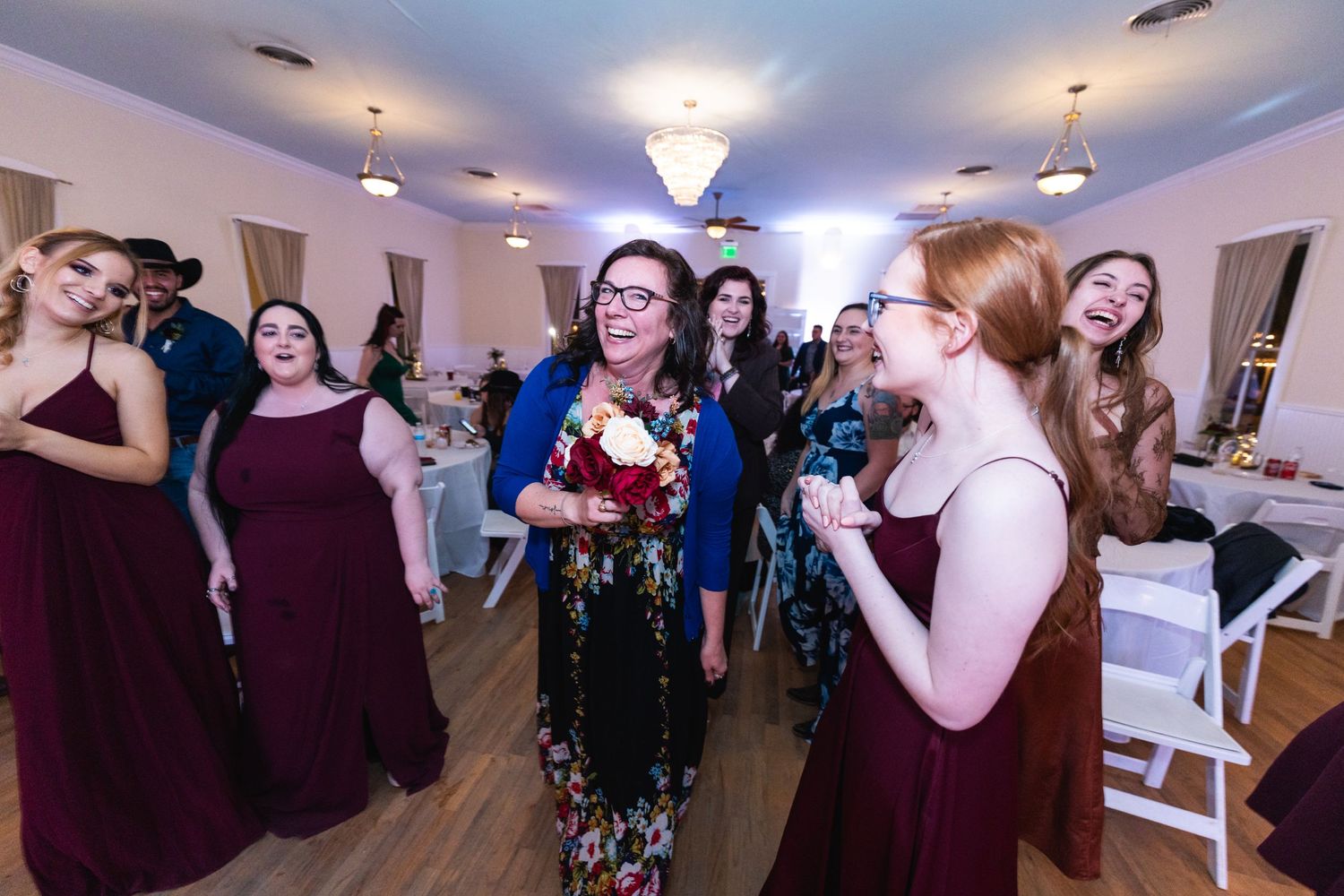 Wedding party members in burgundy dresses gather on the dance floor during the reception.