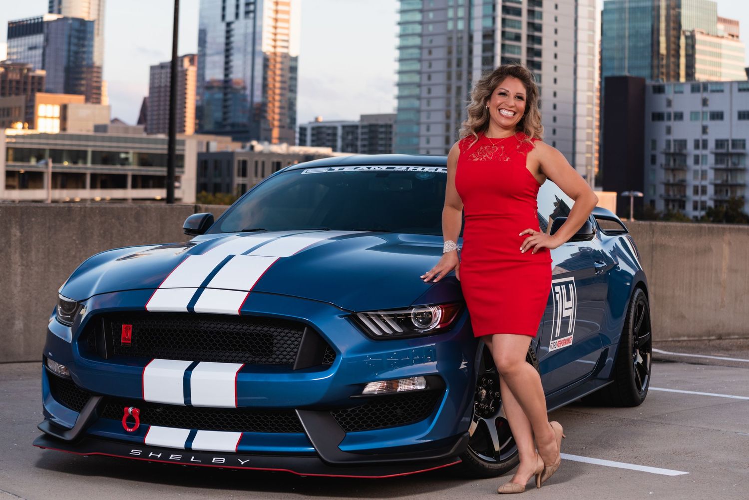 Blue Mustang GT350 with white racing stripes parked in urban rooftop setting.