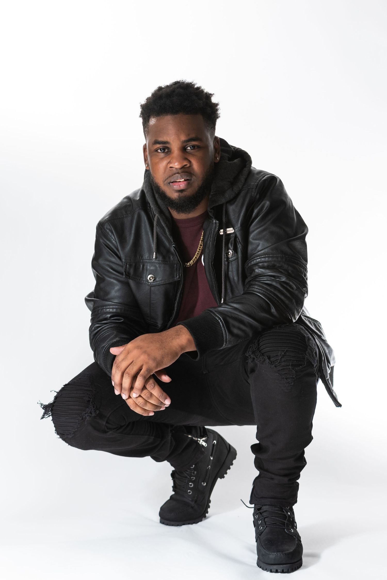 Urban fashion portrait with black leather jacket and distressed jeans in crouching pose.