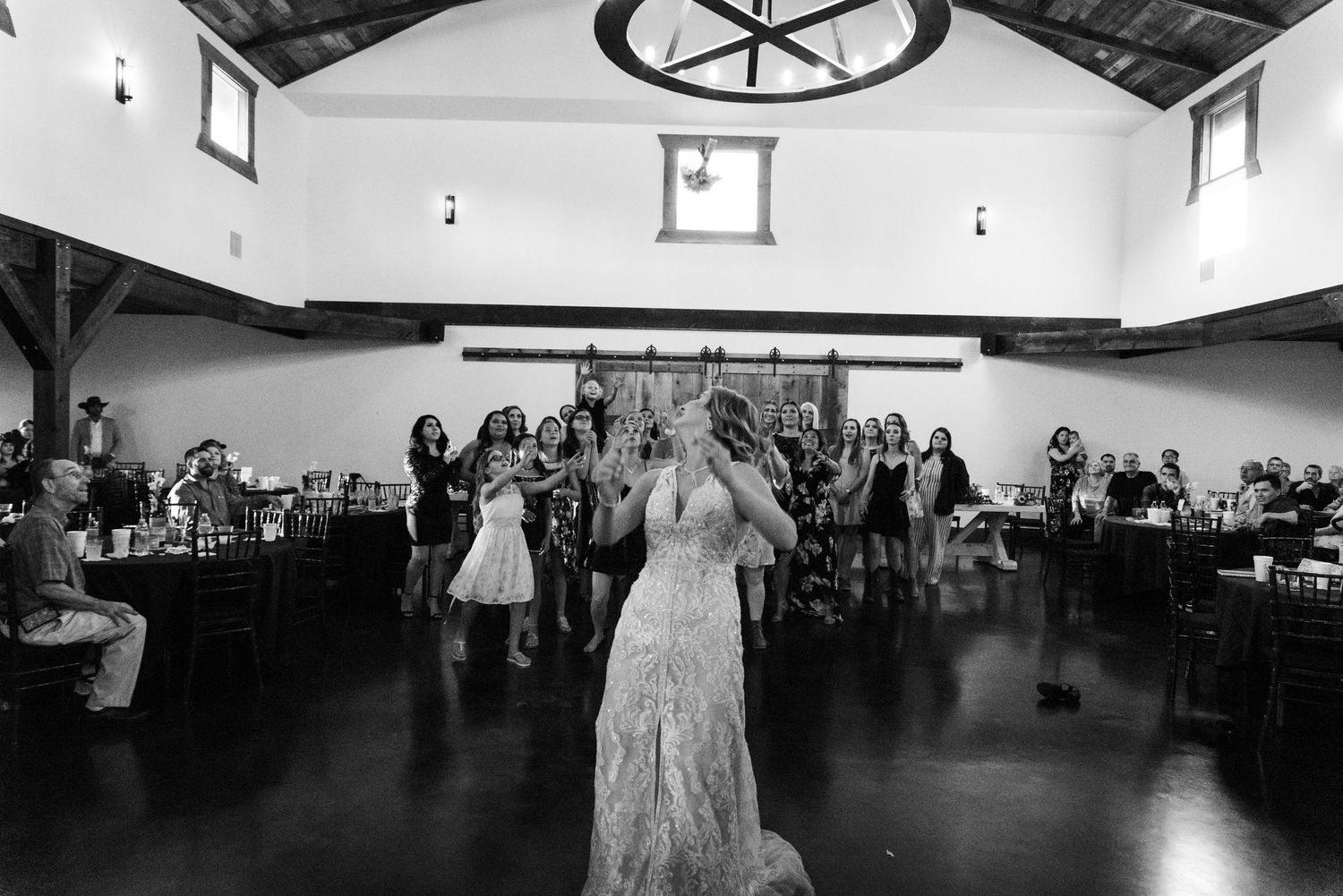 Black and white photo of a bouquet toss moment at a rustic wedding reception venue.