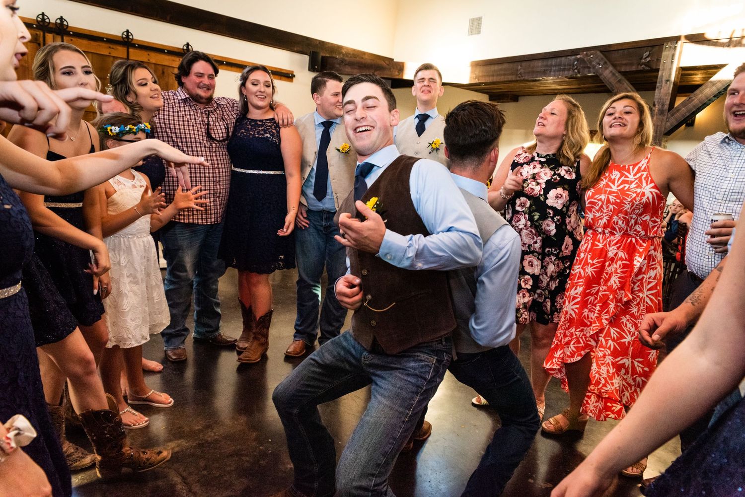 Wedding guests surround dancers performing energetic moves on the reception dance floor.