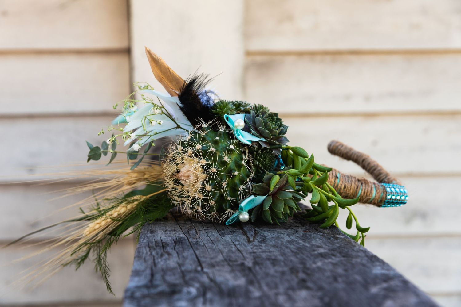 Rustic wedding bouquet with feathers, greenery and blue accents rests on grey surface.