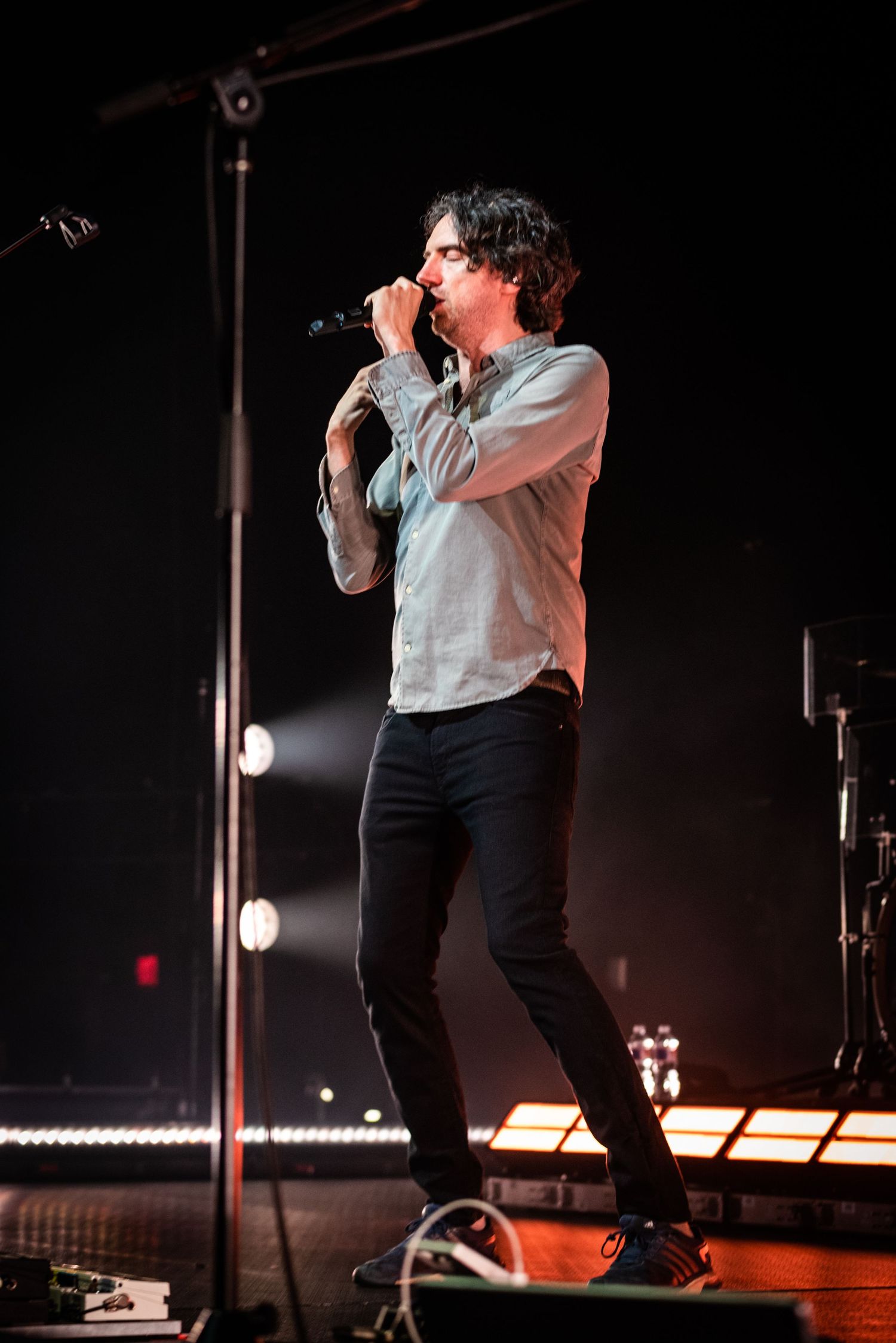 Singer performing on illuminated stage with microphone in hand.