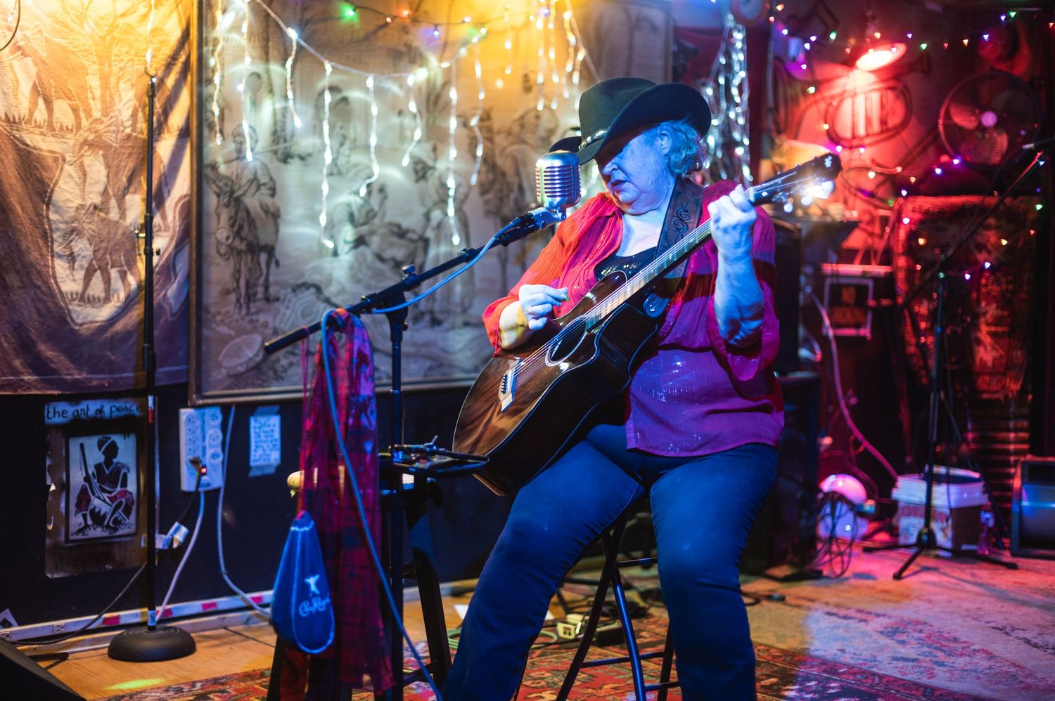 Musicians perform on stage with guitars against a backdrop of string lights and wall decorations.