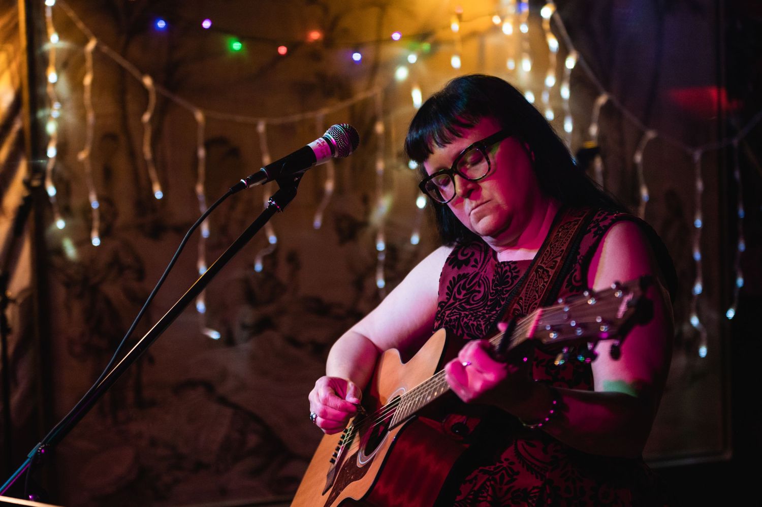 Musician performing with acoustic guitar under colorful stage lights.