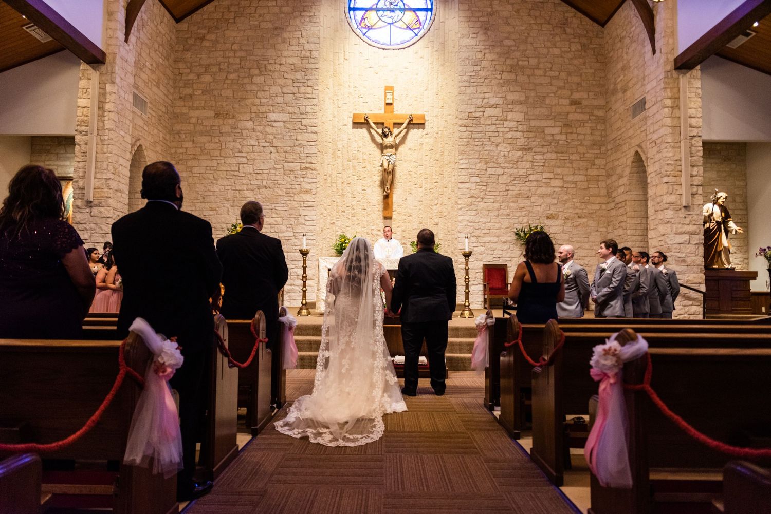 A Catholic wedding ceremony in progress inside a church with stone walls and a large crucifix on display.