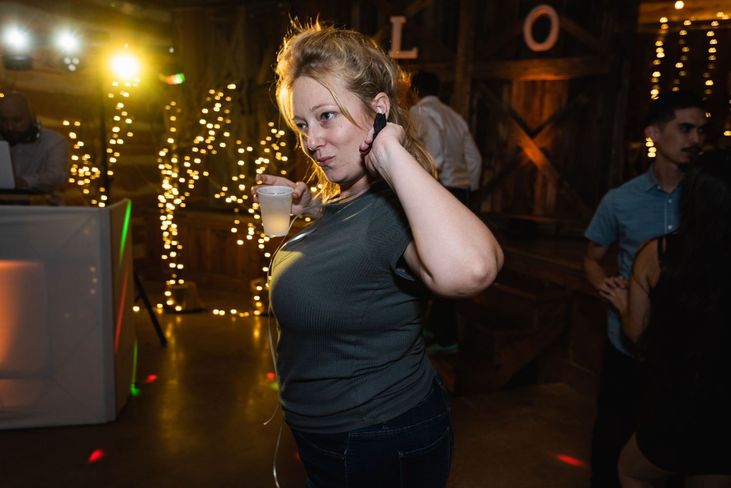 A person dances in a dark venue illuminated by warm string lights in the background.