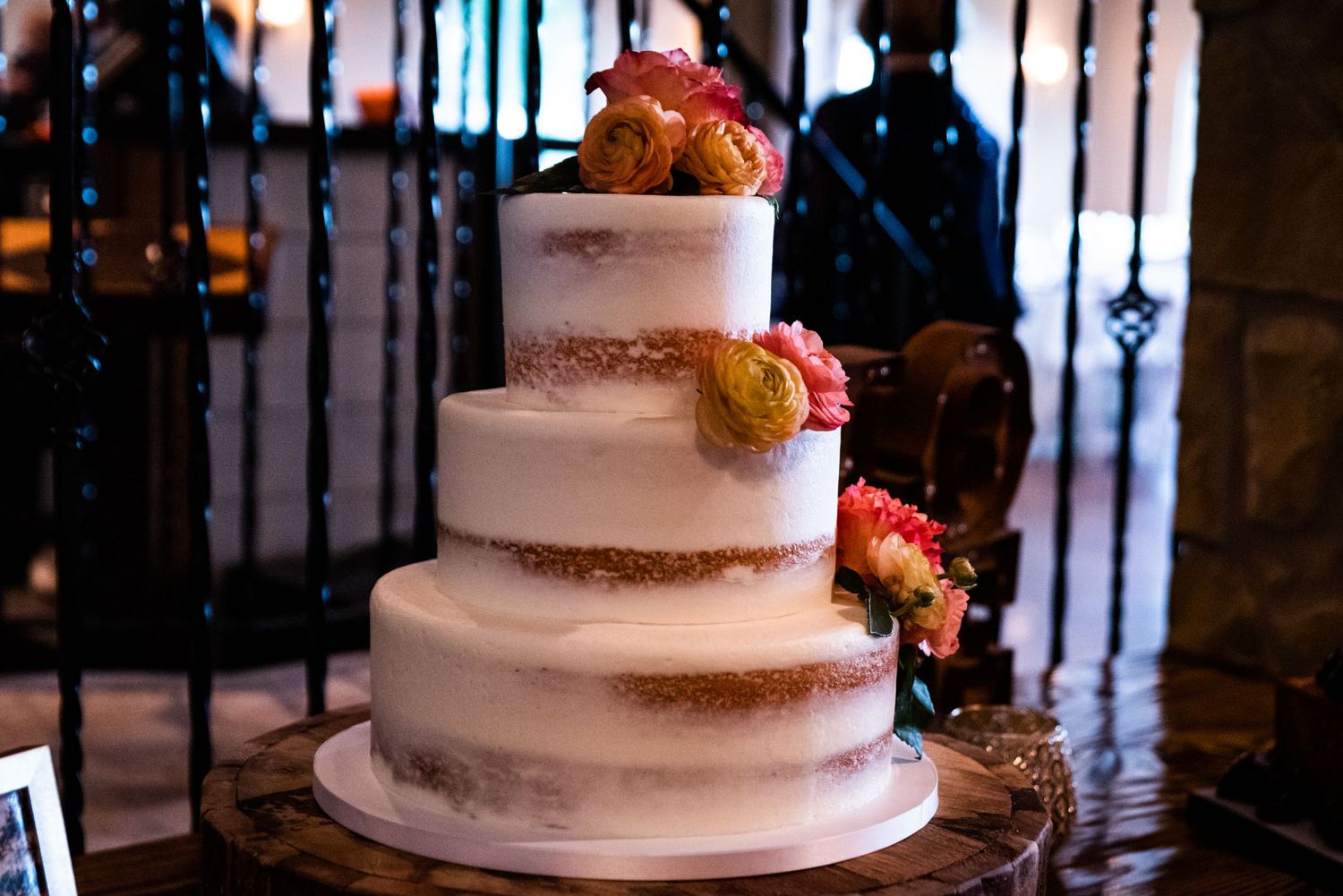 Elegant white tiered wedding cake with fresh flowers displayed against dark iron gates.