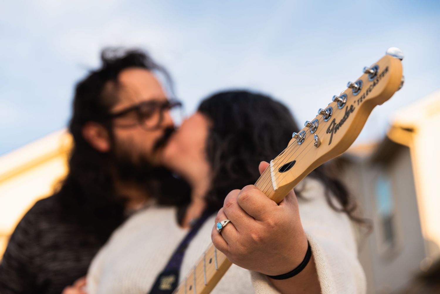 Detailed view of hands holding a Telecaster-style guitar neck against a blue sky.