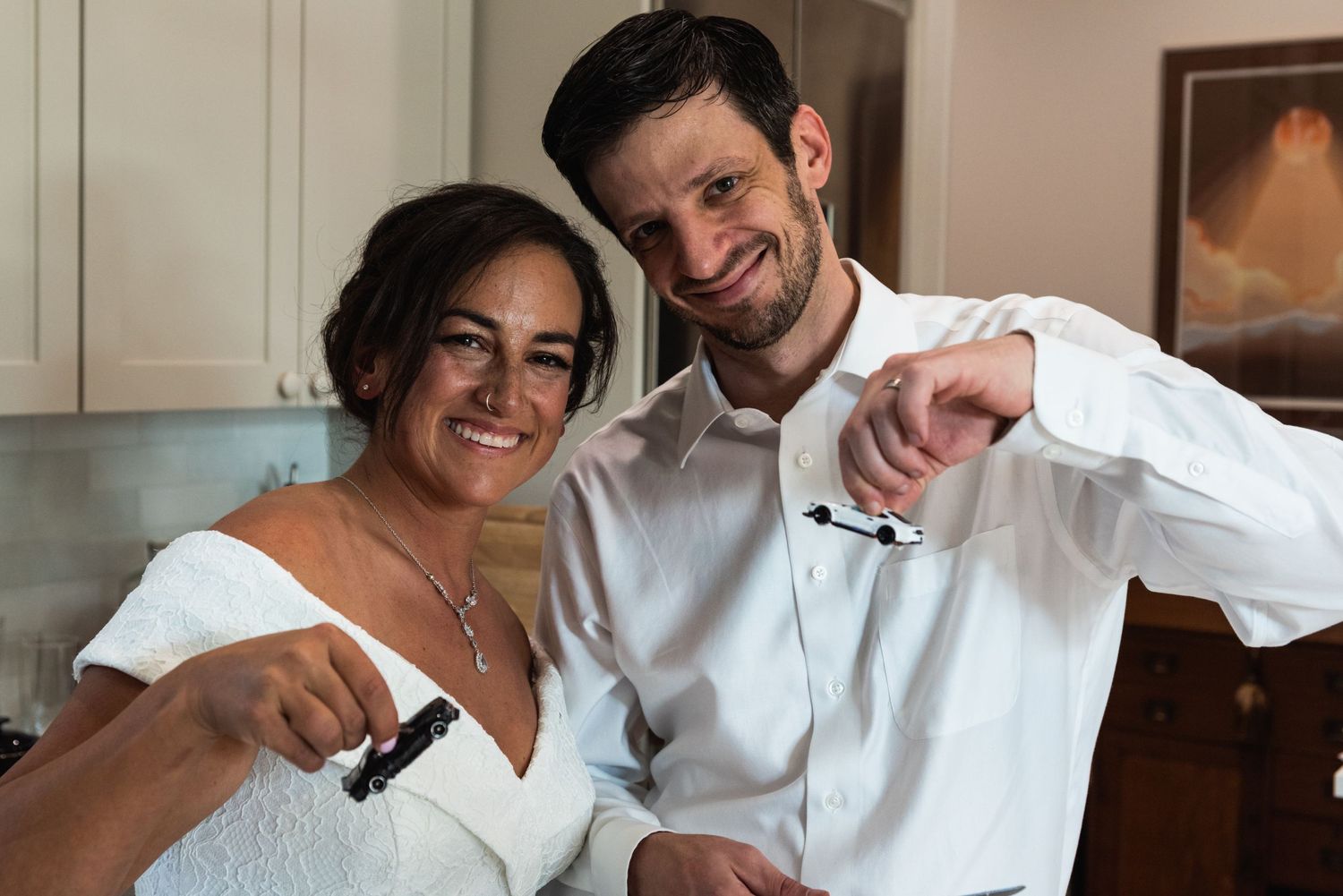 A couple raises wine glasses in celebration while wearing white wedding attire.