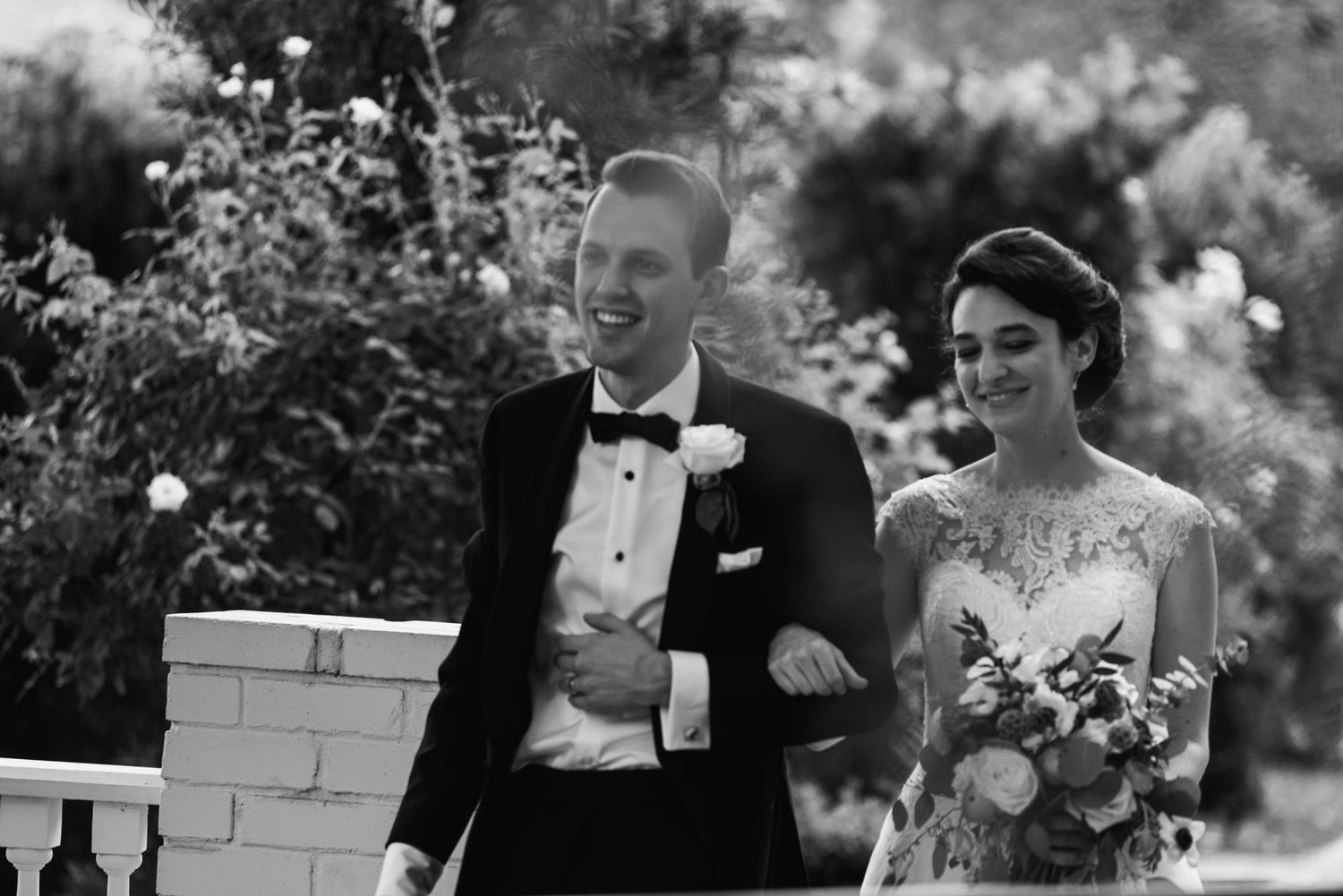 A black and white wedding portrait capturing a candid moment in a garden setting.