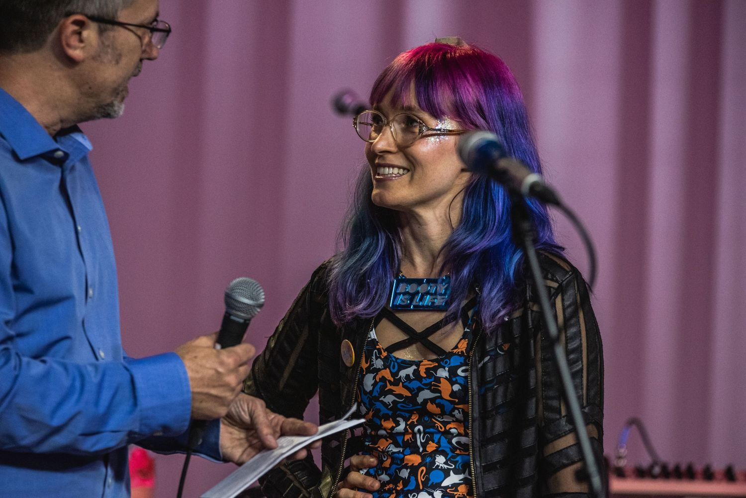 Interview with musician in patterned dress against pink stage curtain.
