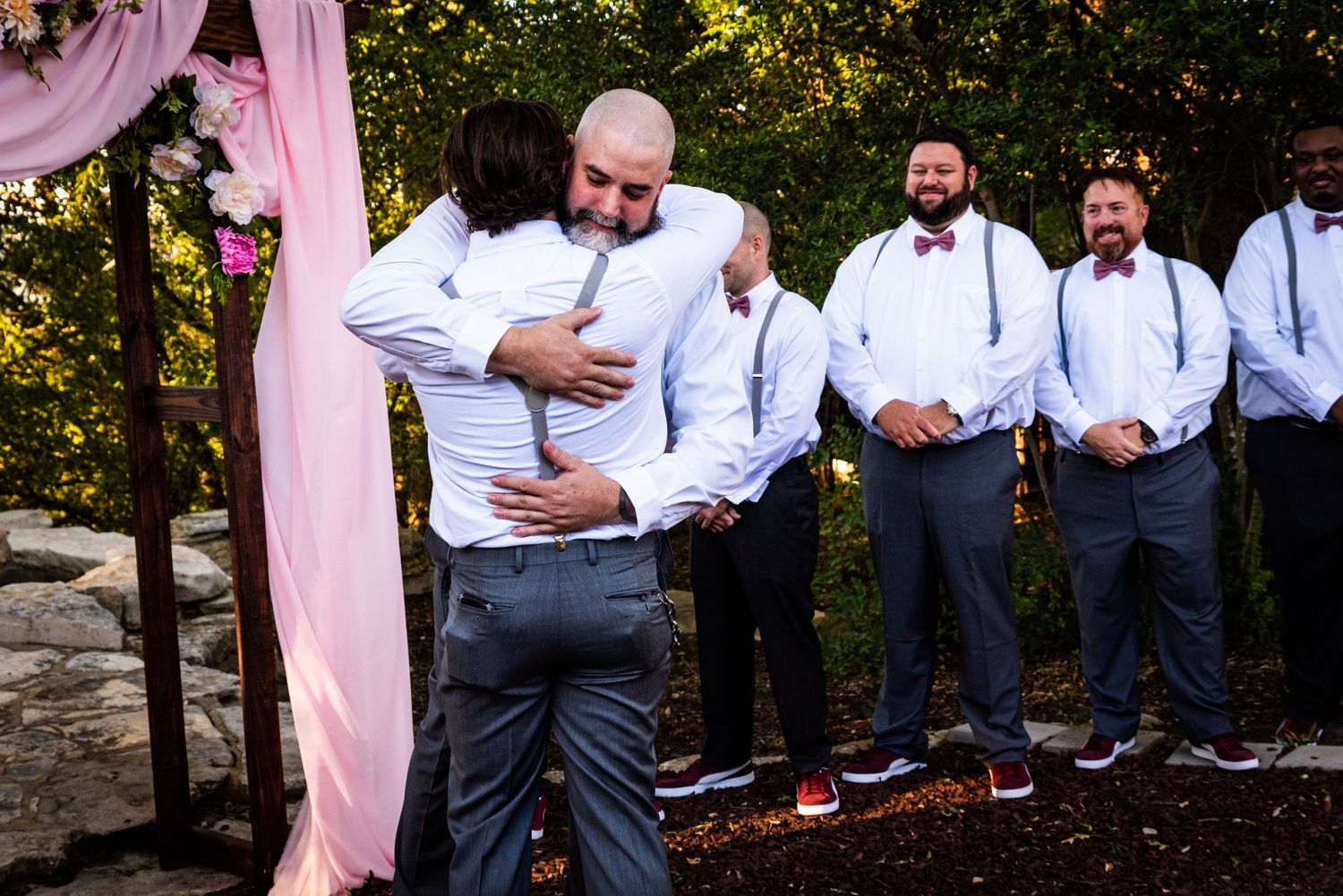 An emotional embrace during a wedding ceremony with groomsmen standing in background.