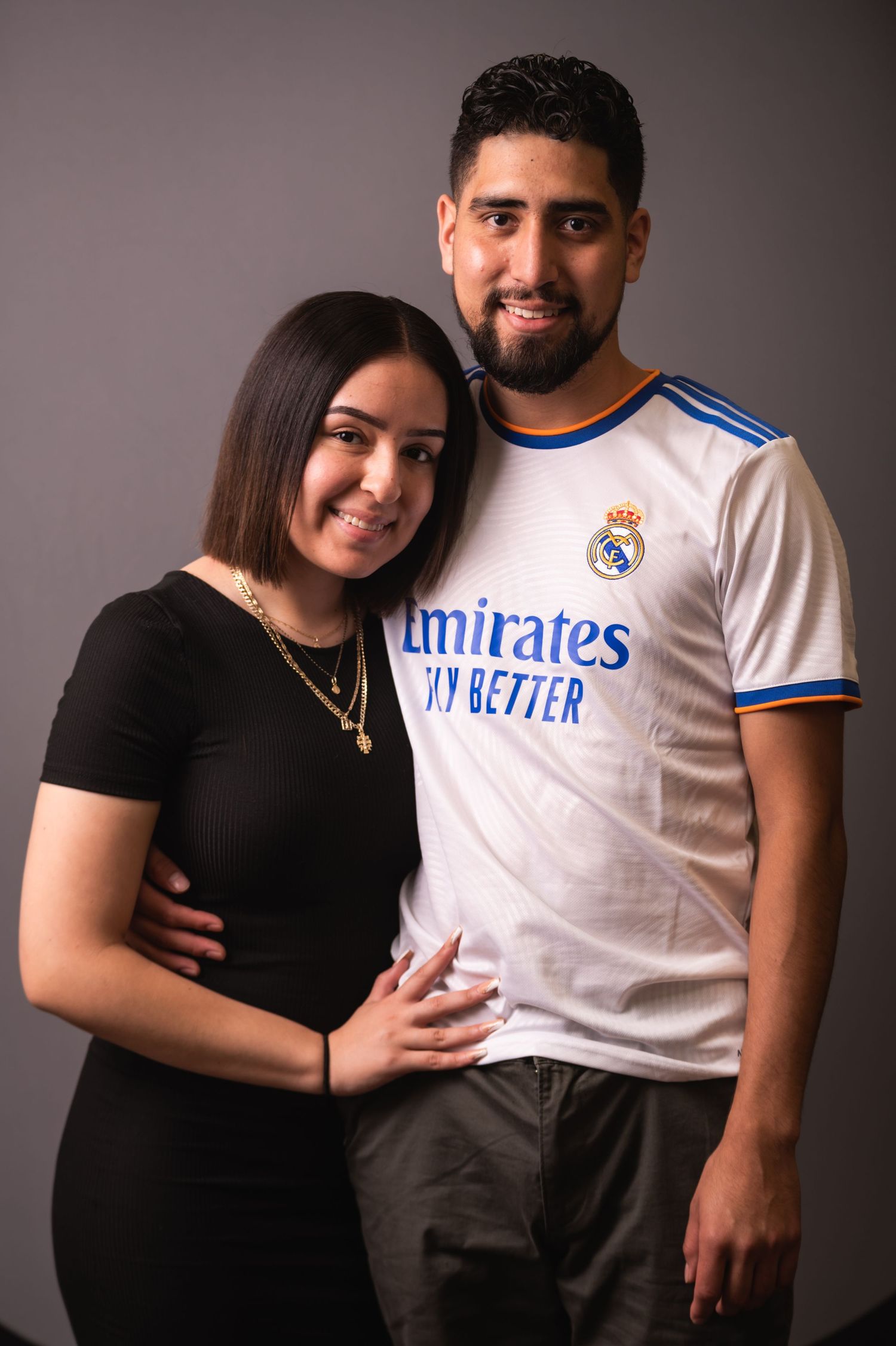 Couple posing together, with one wearing Real Madrid jersey and the other in black top.