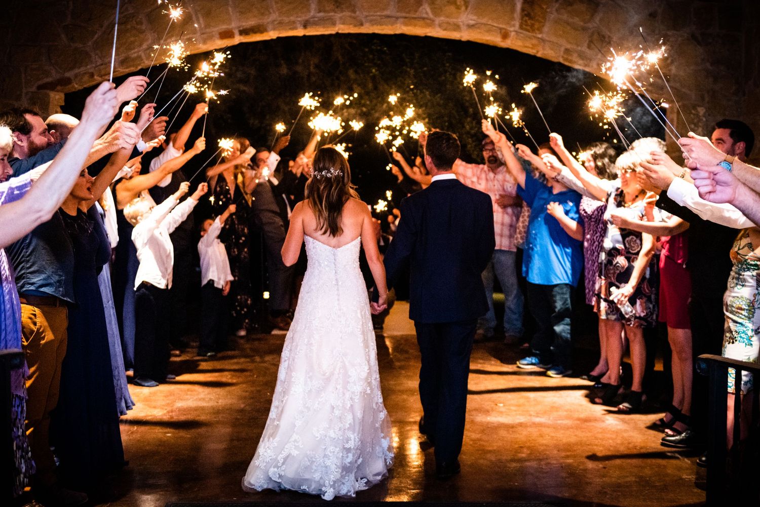Wedding guests create a magical sparkler tunnel exit for the newlyweds at an evening celebration.