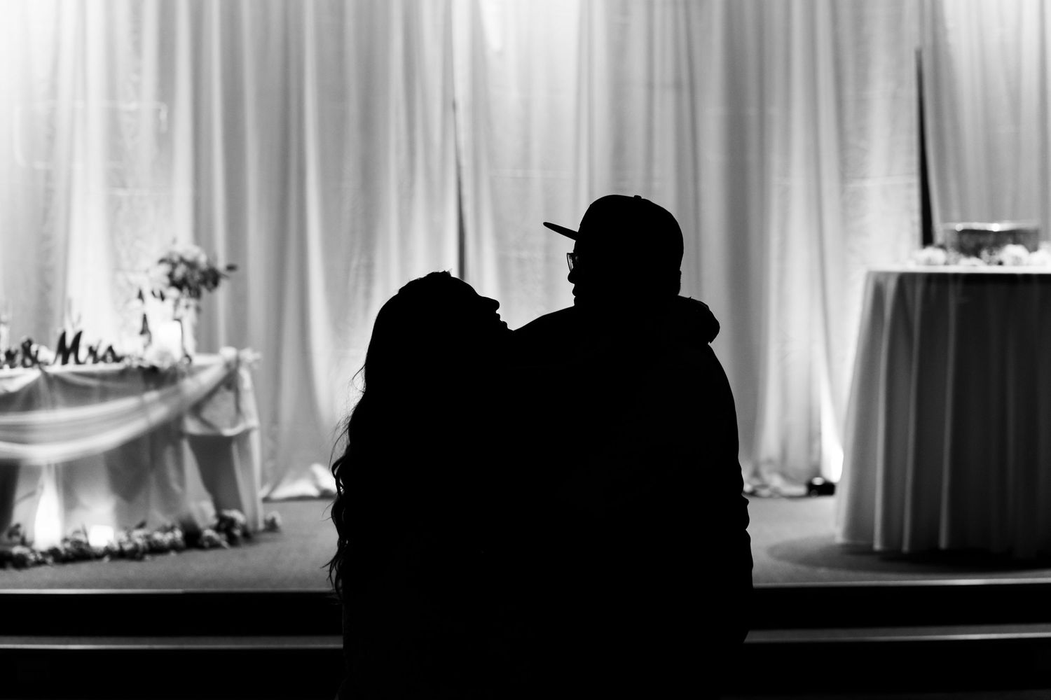 Silhouette of a couple embracing near decorated tables at an evening wedding reception.