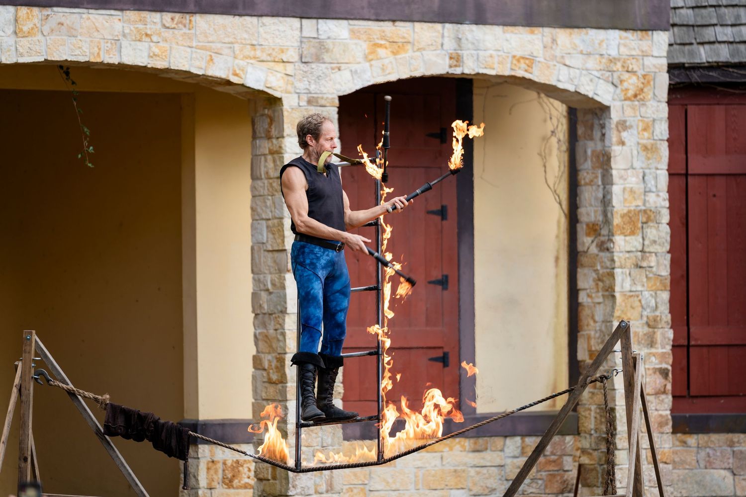 A skateboarder performs an ollie trick in front of an arched stone entrance with wooden shutters.