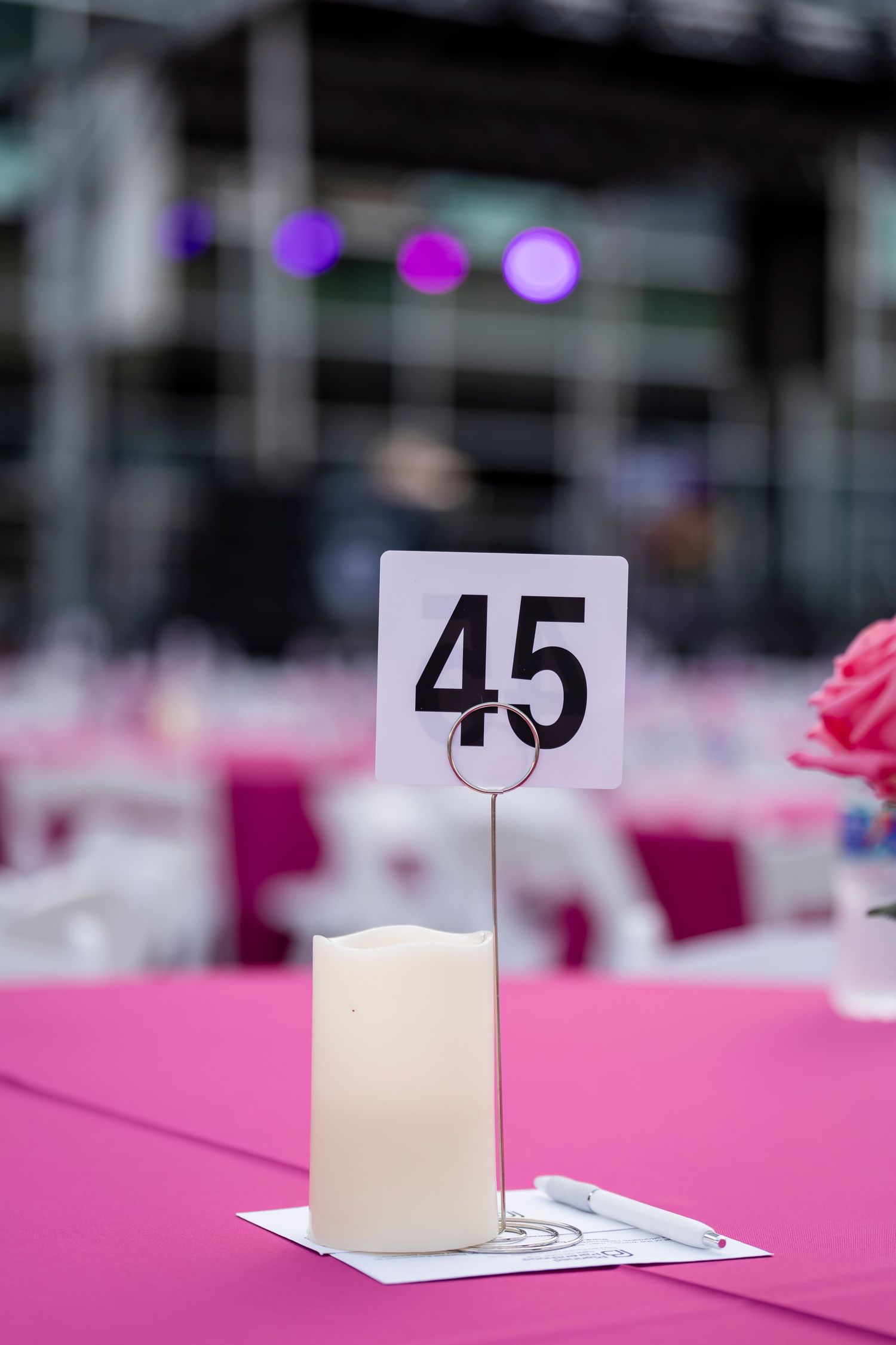 Table number forty-five card holder in white sits on pink tablecloth at formal event setting.
