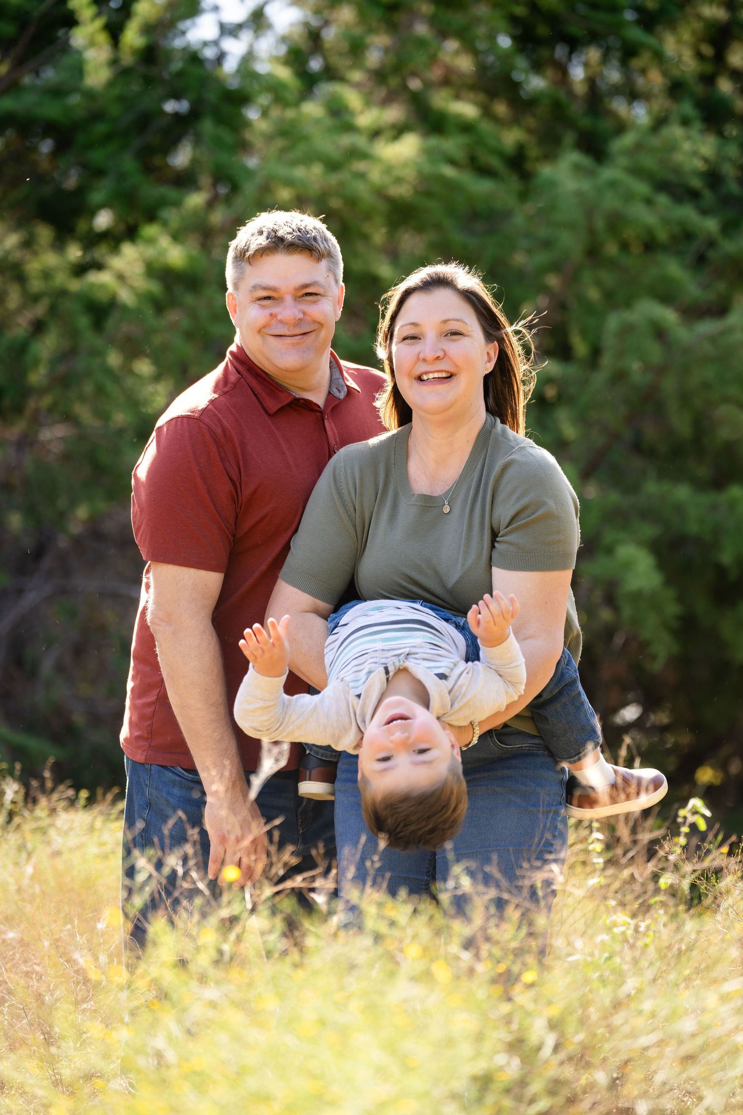Family plays and laughs together in a sunny field with golden grass during outdoor photo session.