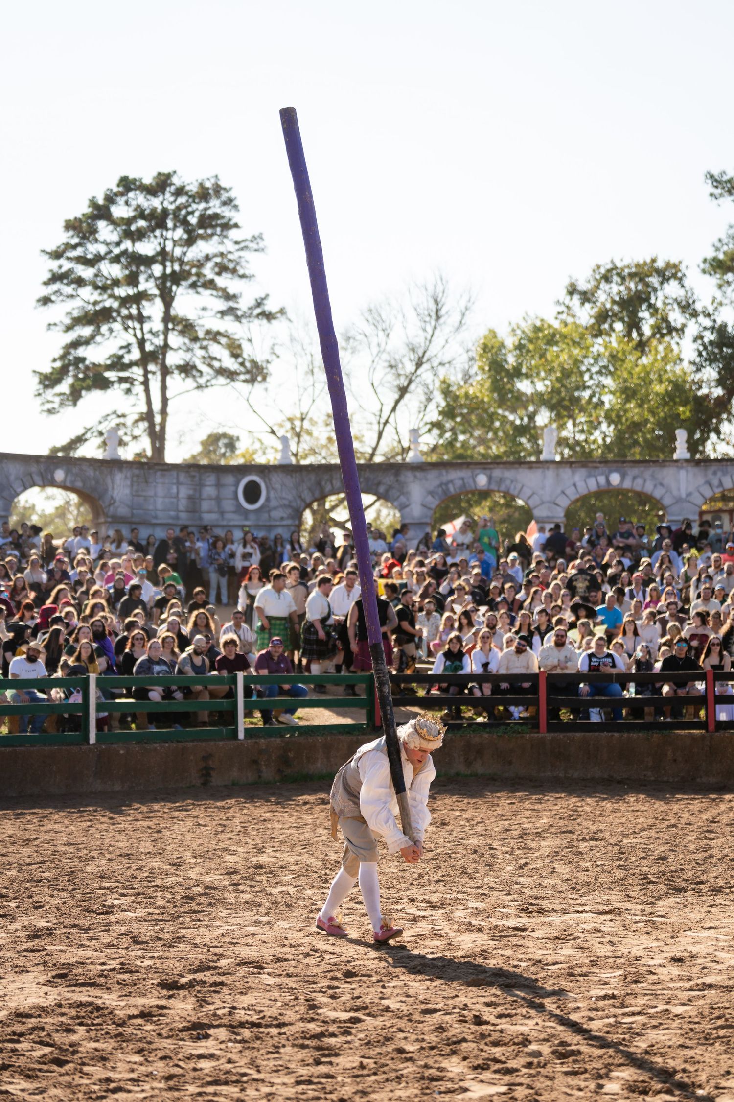 Two performers demonstrate martial arts moves in a dirt arena surrounded by a large outdoor crowd.