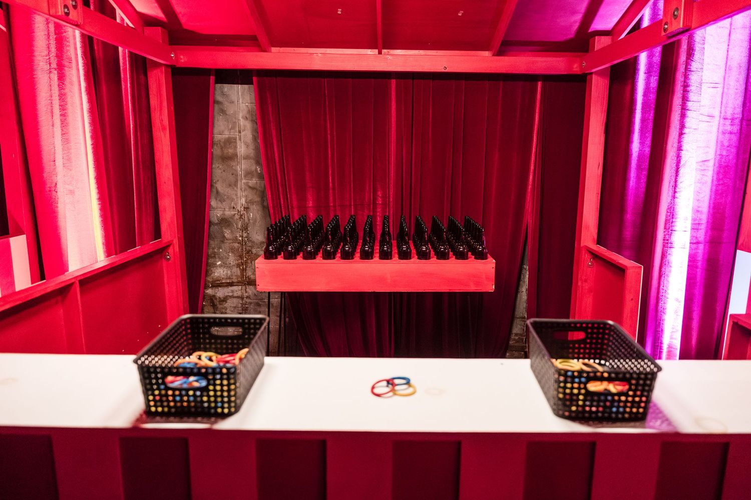Pink and magenta lighting illuminates an empty theater stage with black chairs arranged in rows.