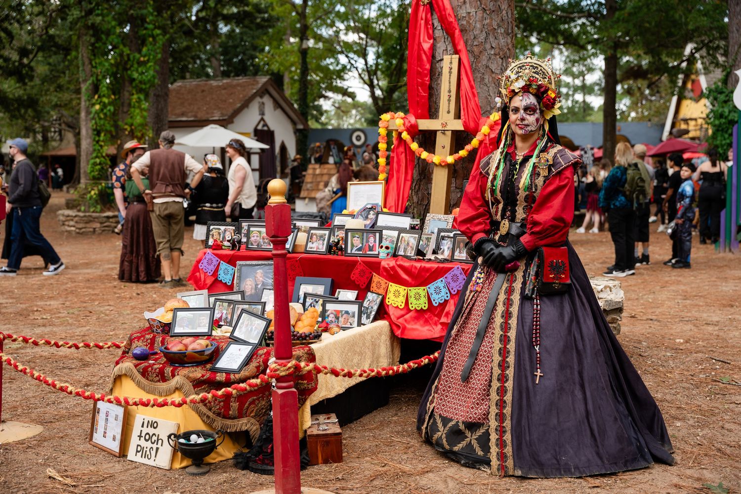Vendors in medieval costumes display their wares at a renaissance festival marketplace with red banners and tents.