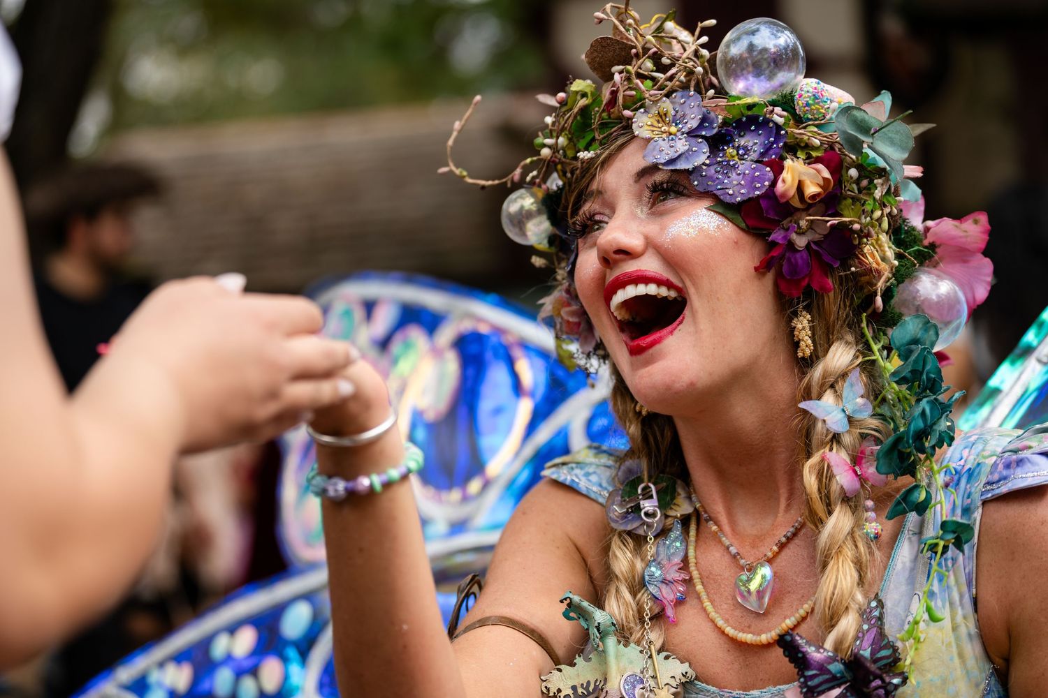 A group of people in floral dresses and flower crowns celebrate joyfully at a summer party.