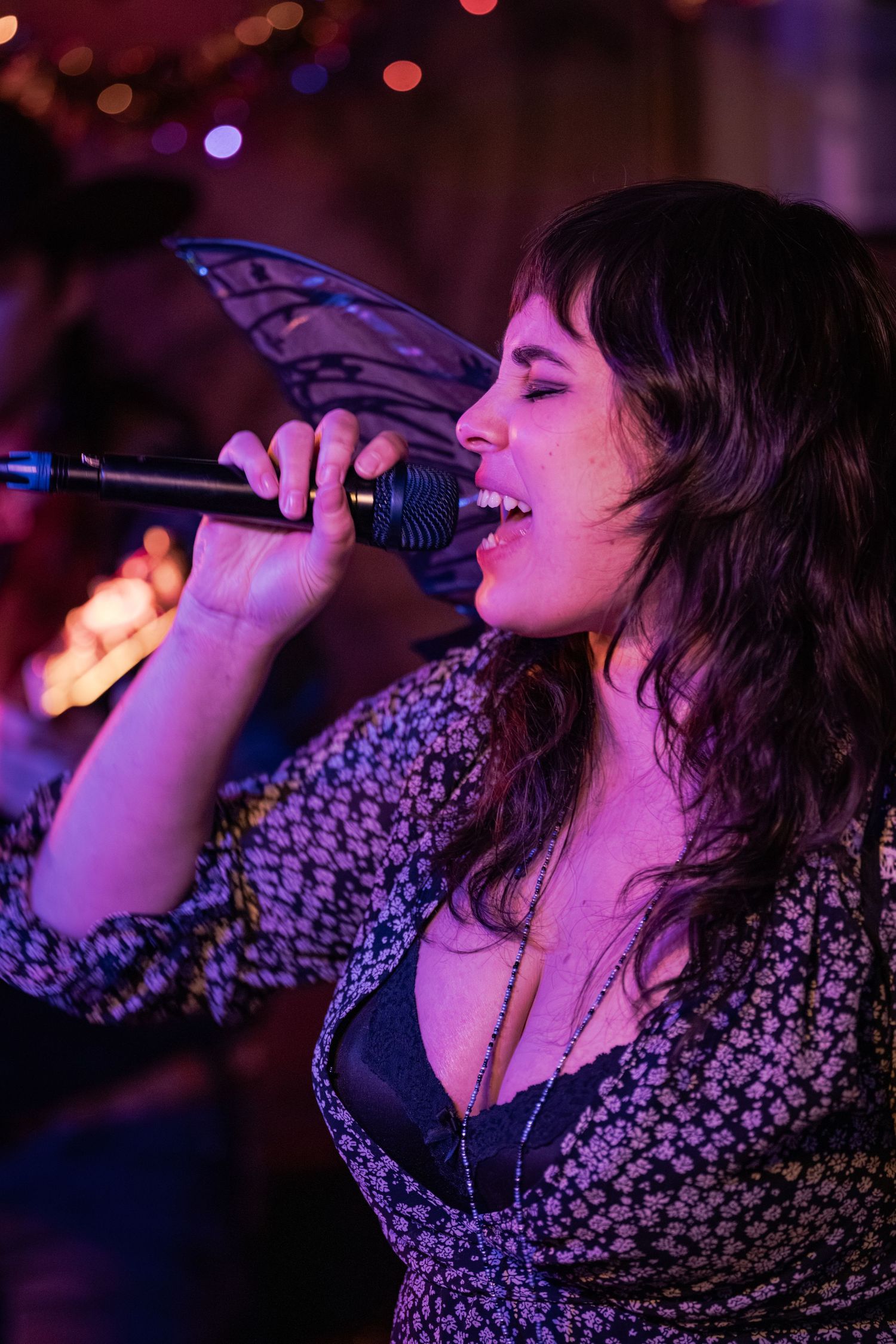 A singer performs passionately on stage with a microphone under purple lighting at a live music venue.