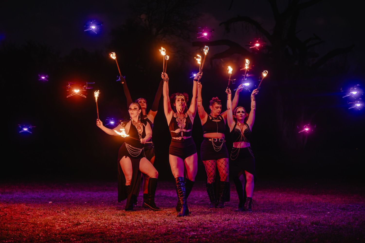 Five performers in black costumes hold flaming torches during a dramatic outdoor fire dance show at night.