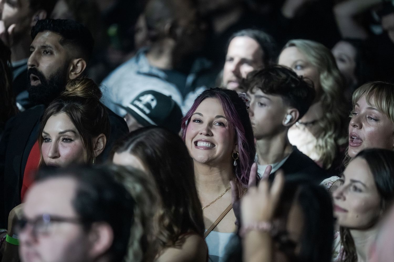 Smiling woman with pink hair enjoys a live concert surrounded by an engaged crowd.