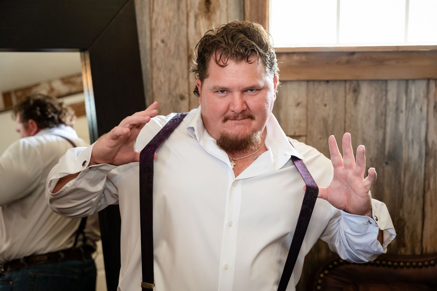 Man in white shirt and purple suspenders posing playfully indoors at a rustic wooden venue.