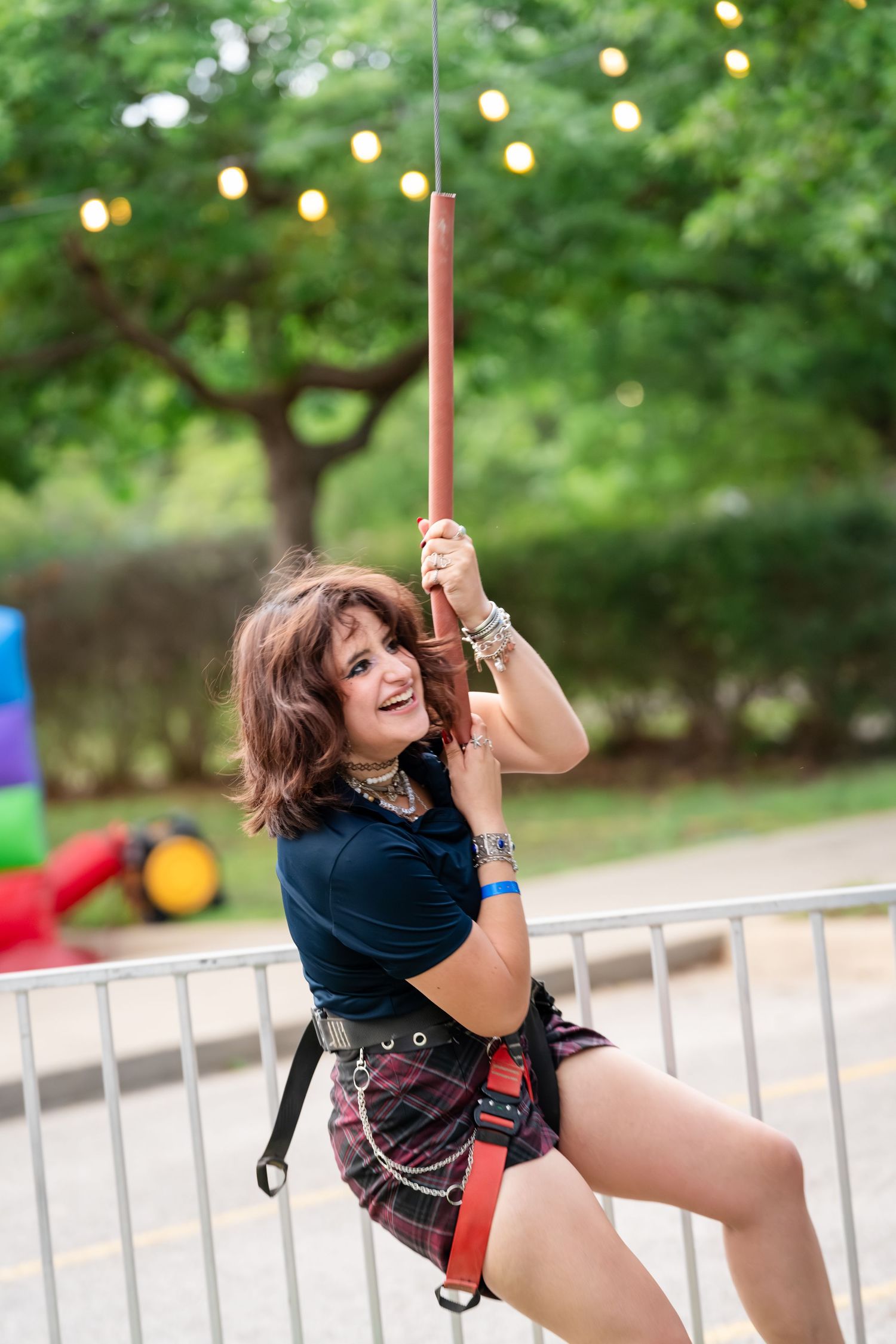 Smiling woman in plaid skirt and harness climbing a rope at an outdoor adventure activity area.