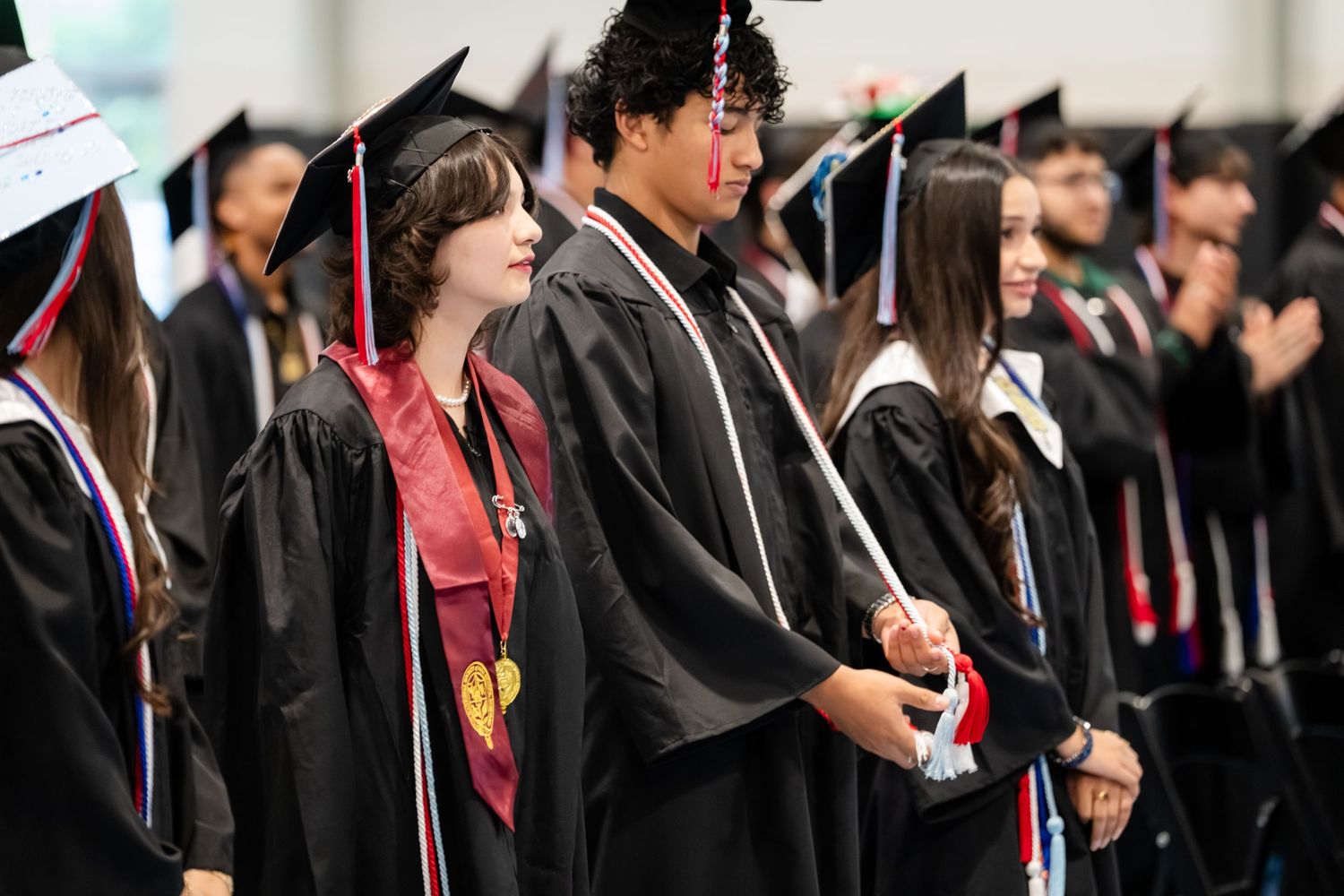 Students in black graduation gowns and caps stand together during a commencement ceremony.