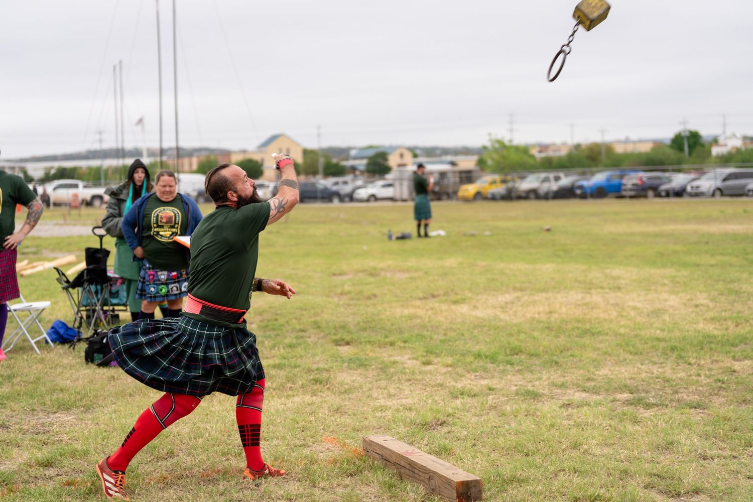 Man in kilt throwing weight over bar at Highland Games competition on grassy field.