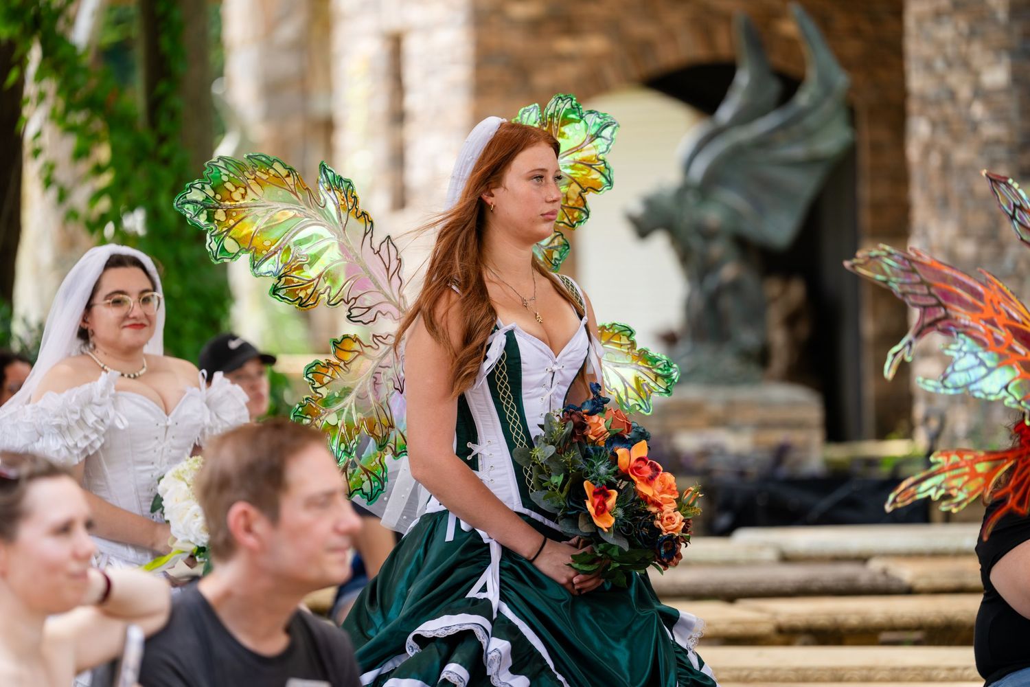 Women in fairy costumes with green wings and a dragon statue at a Renaissance festival.