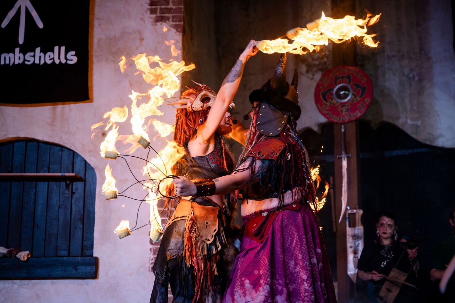 A performer spins flaming props in a dramatic fire dance performance at night.