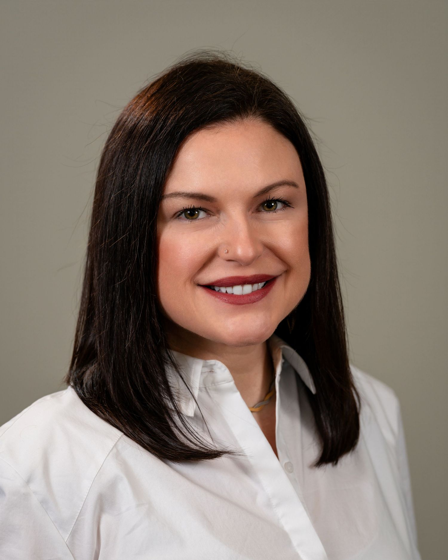 Professional headshot of a smiling woman with dark hair wearing a white blouse against a gray background.