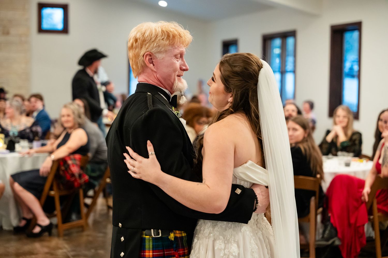 Bride and groom share first dance at wedding reception, groom wearing traditional Scottish kilt.