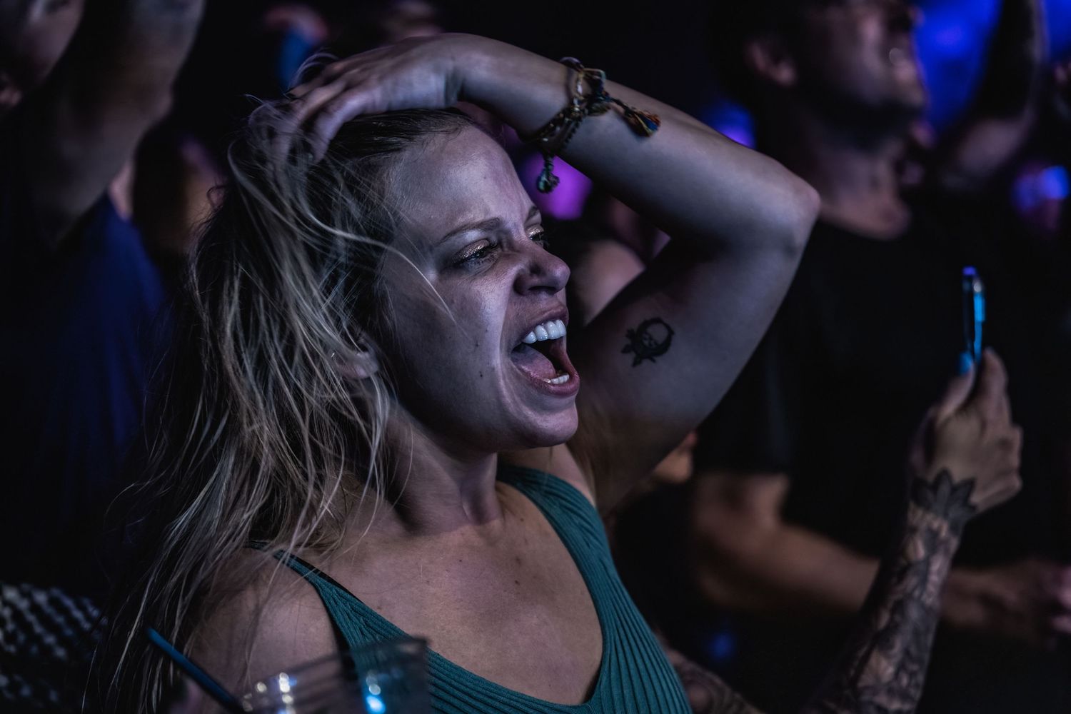 A person laughs joyfully during a live performance in a dark concert venue with blue lighting.